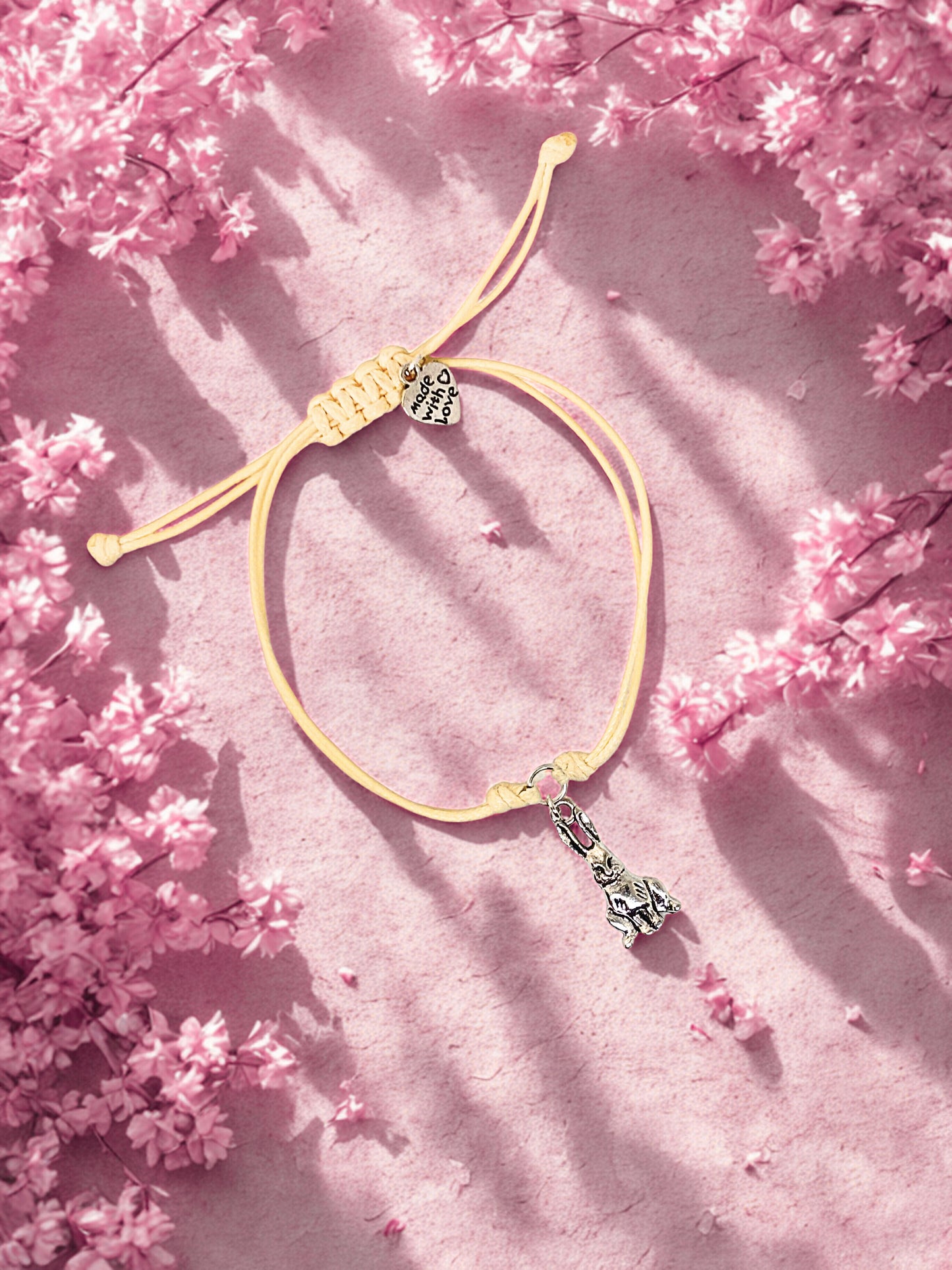Beige cord bracelet with a bunny charm on a pink floral background