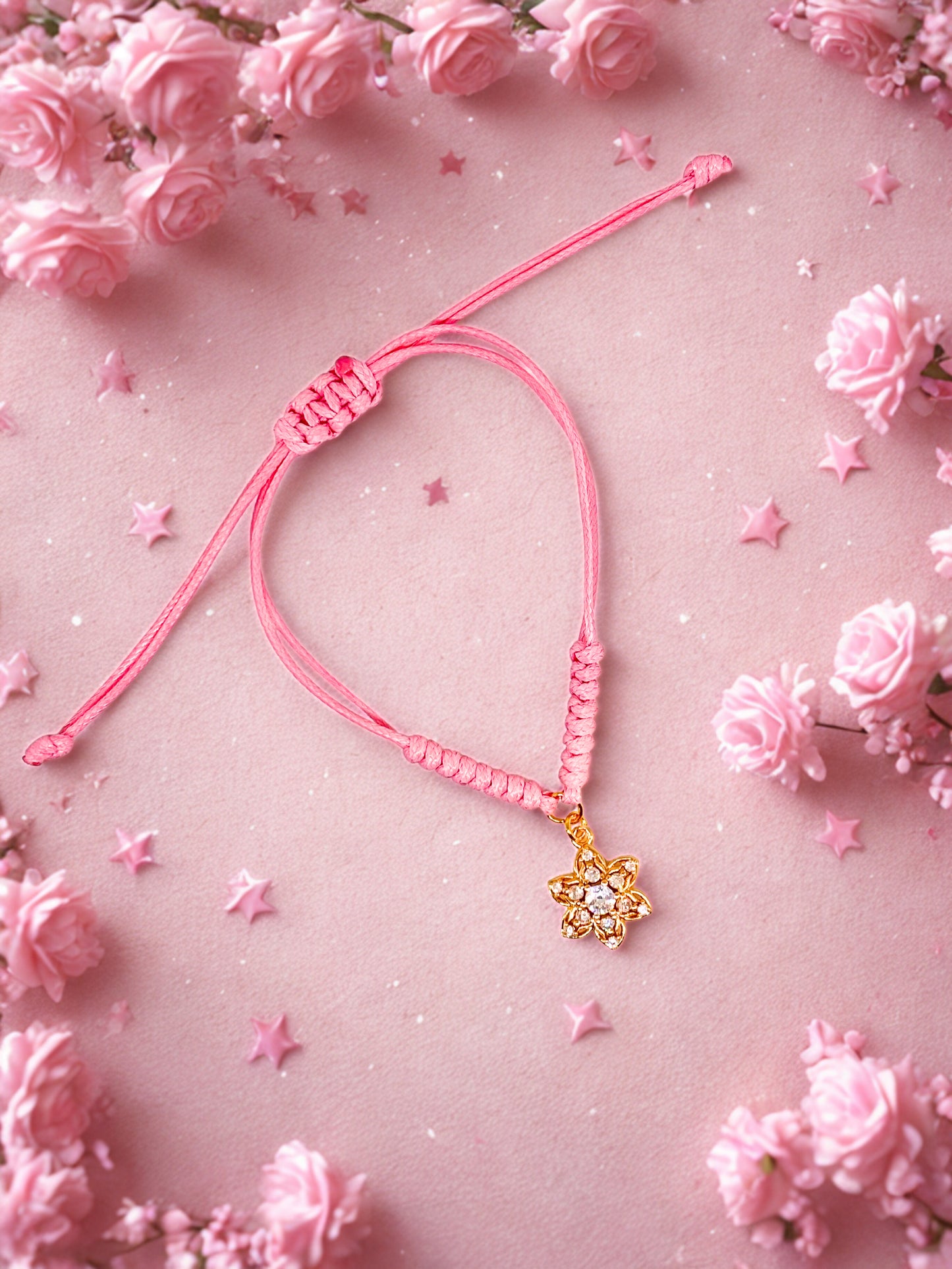 Pink braided bracelet with a flower shaped charm on a pink floral background