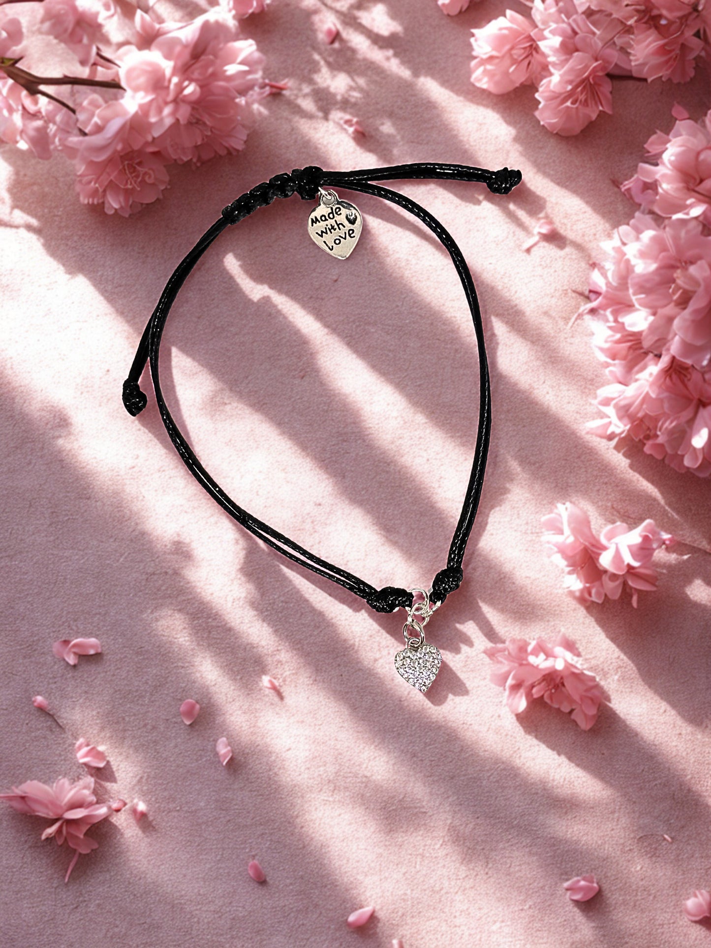 Black cord bracelet with heart-shaped charms on a pink floral background