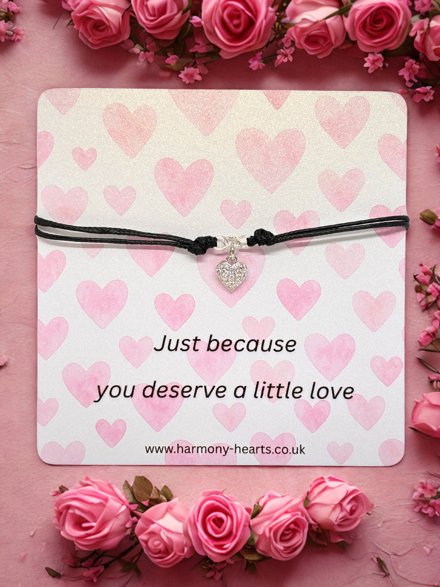 Bracelet with a heart charm on a pink heart-patterned card surrounded by pink roses.