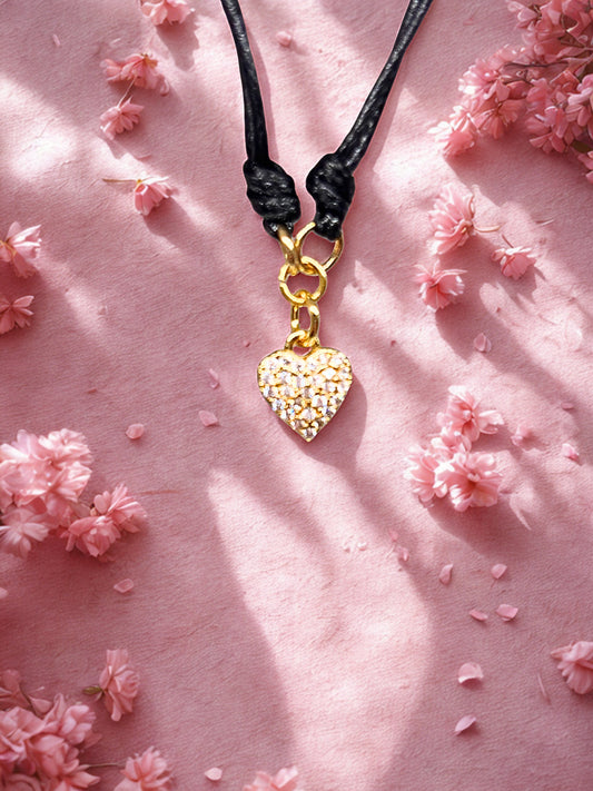 Gold heart-shaped charmt on a black cord against a pink floral background