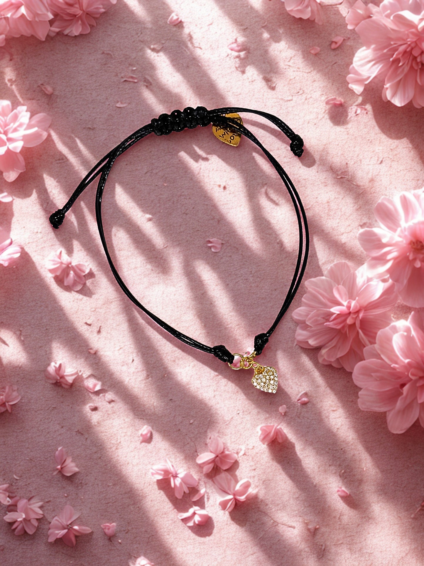 Black cord bracelet with a gold charm on a pink floral background