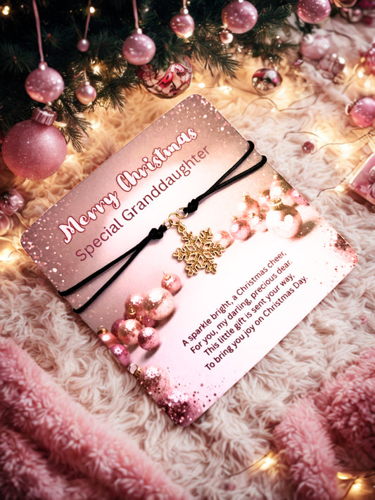 Card with gold snowflake bracelet and text 'Merry Christmas Special Granddaughter' in front of a decorated Christmas tree.