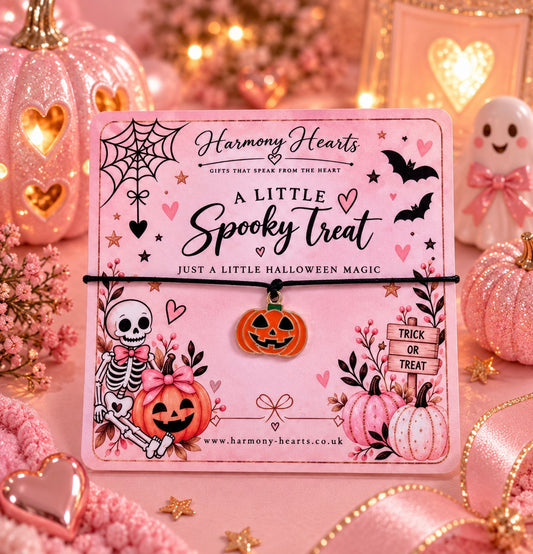 A pink Halloween-themed card from Harmony Hearts holding a black cord bracelet with an orange pumpkin charm. The card is decorated with cute spooky illustrations including a skeleton, pumpkins, bats, and hearts.