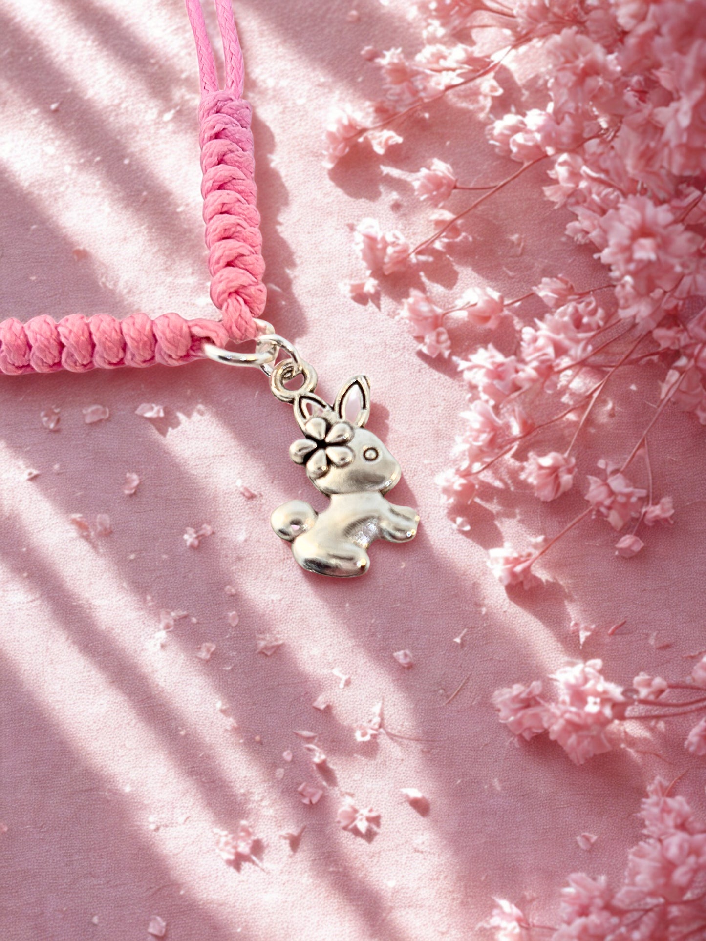 Pink braided bracelet with a silver bunny charm on a pink floral background