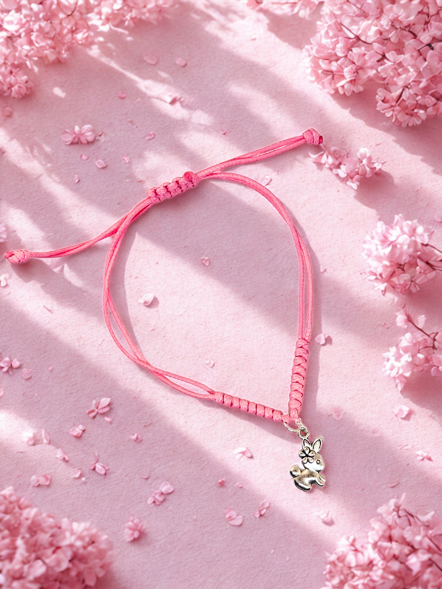 Pink braided bracelet with a silver bunny charm on a pink floral background