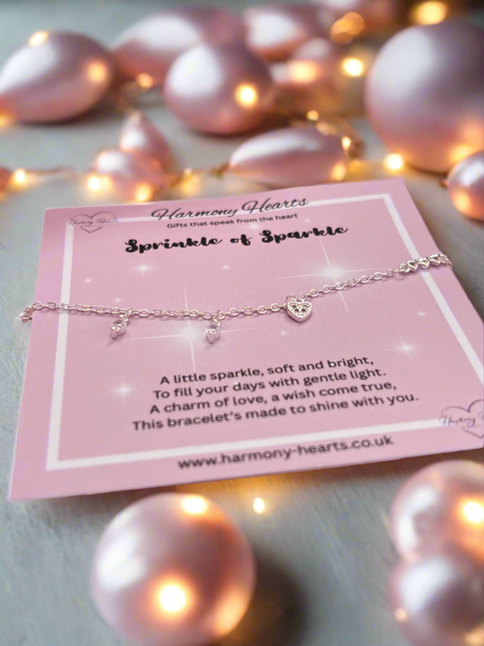 Silver bracelet with heart charm on a pink card with 'Harmony Hearts' branding, surrounded by pink pearls.