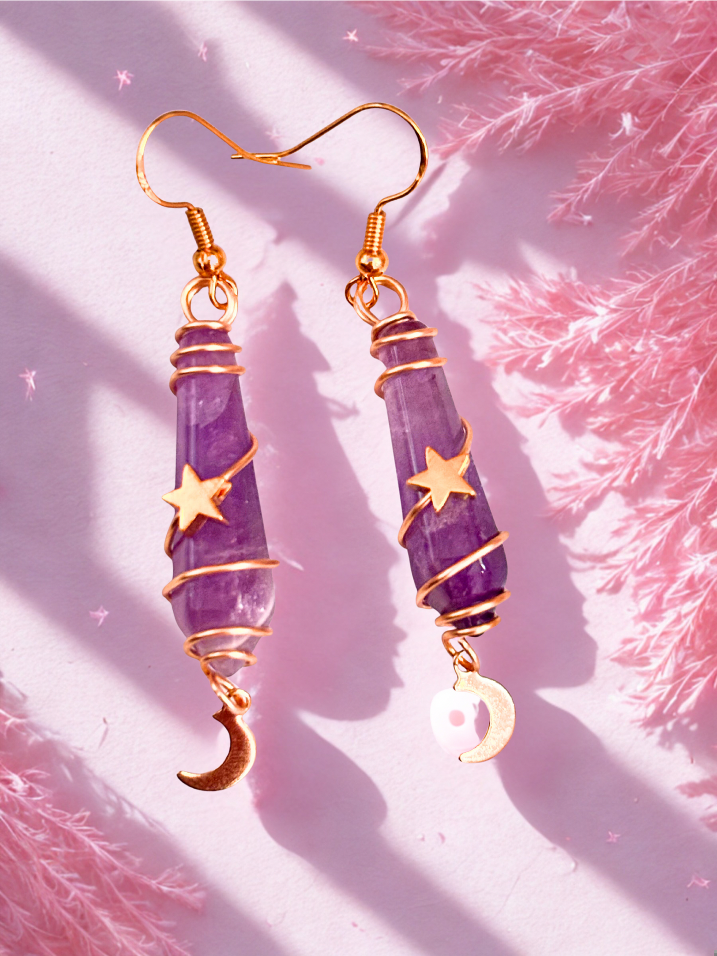 Purple amethyst earrings with gold accents on a pink textured background