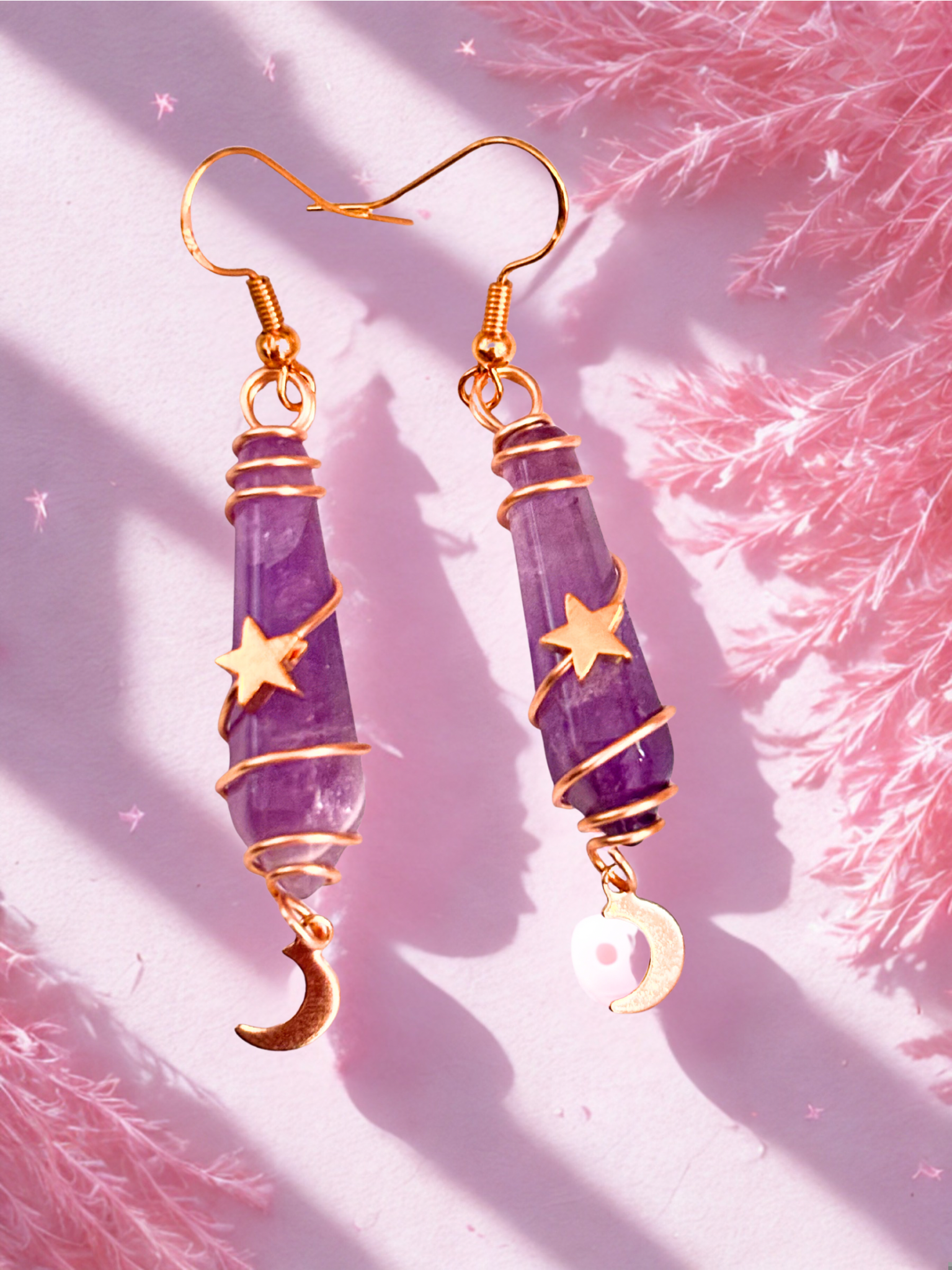 Purple amethyst earrings with gold accents on a pink textured background