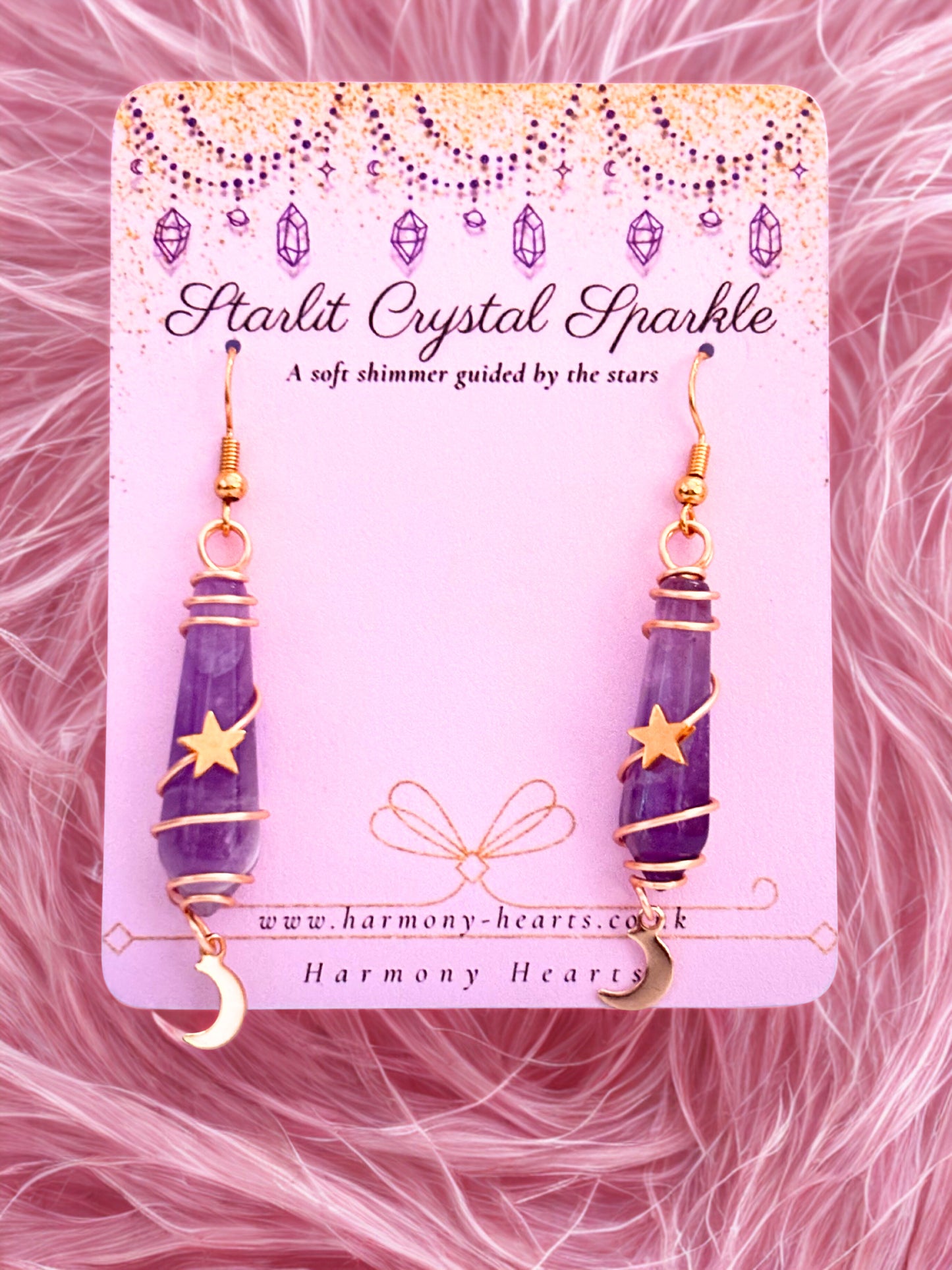 Purple amethyst crystal earrings on a pink card with 'Harmony Hearts' branding against a pink fur background.