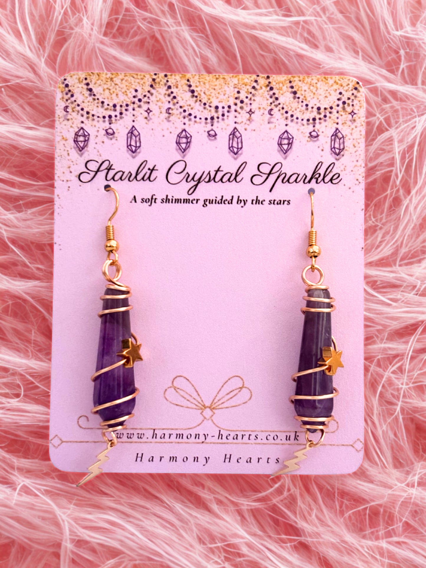 Purple amethyst crystal earrings on a 'Starlit Crystal Sparkle' card with pink faux fur background