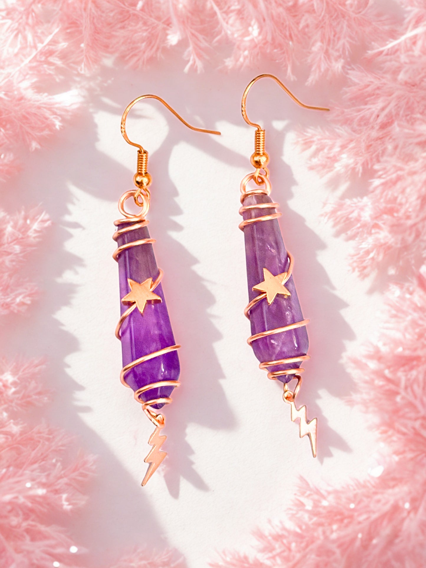 Purple amethyst earrings with gold accents on a pink textured background