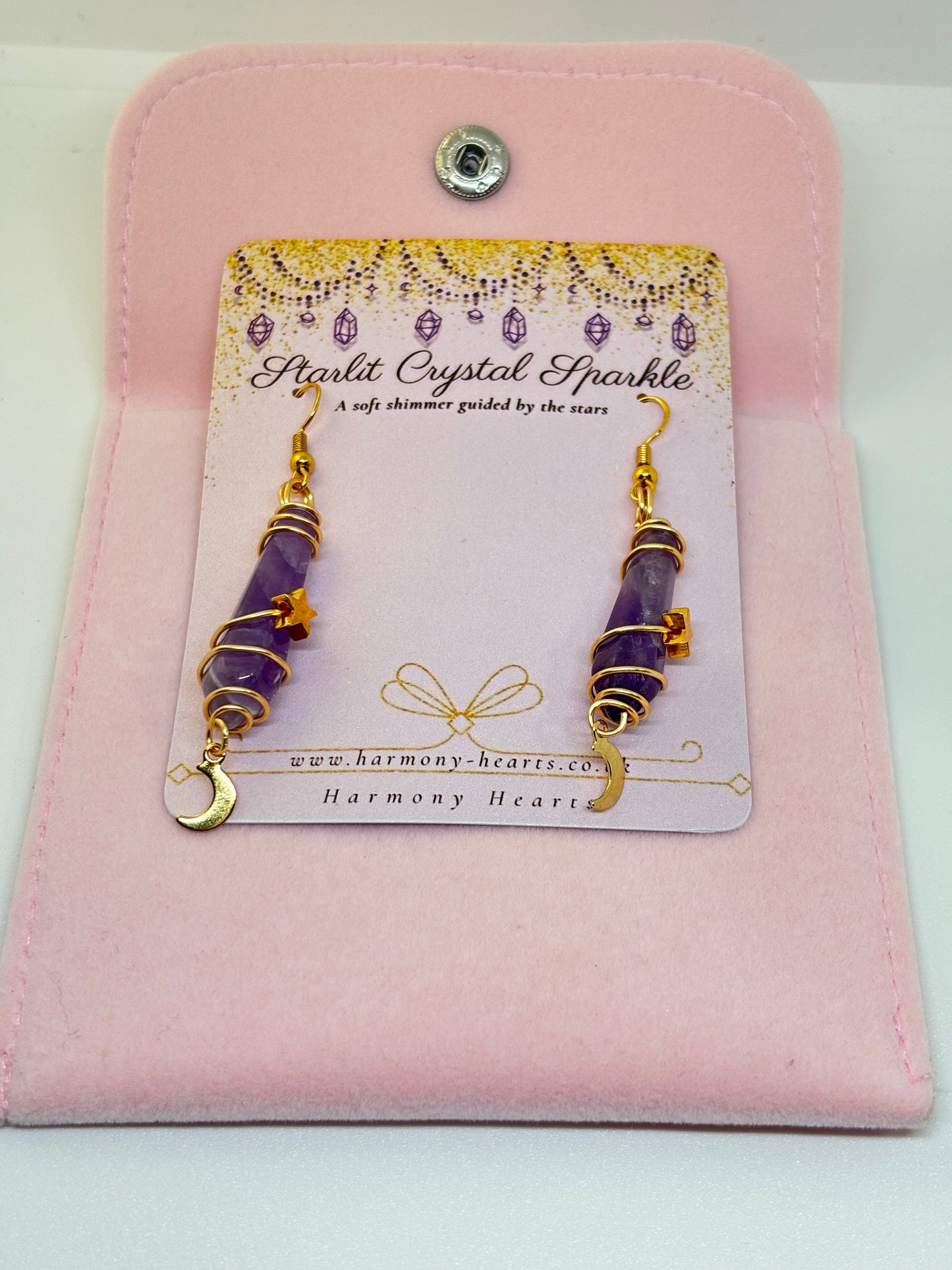 Pair of purple and gold earrings on a 'Harmony Hearts' card with pink display stand.