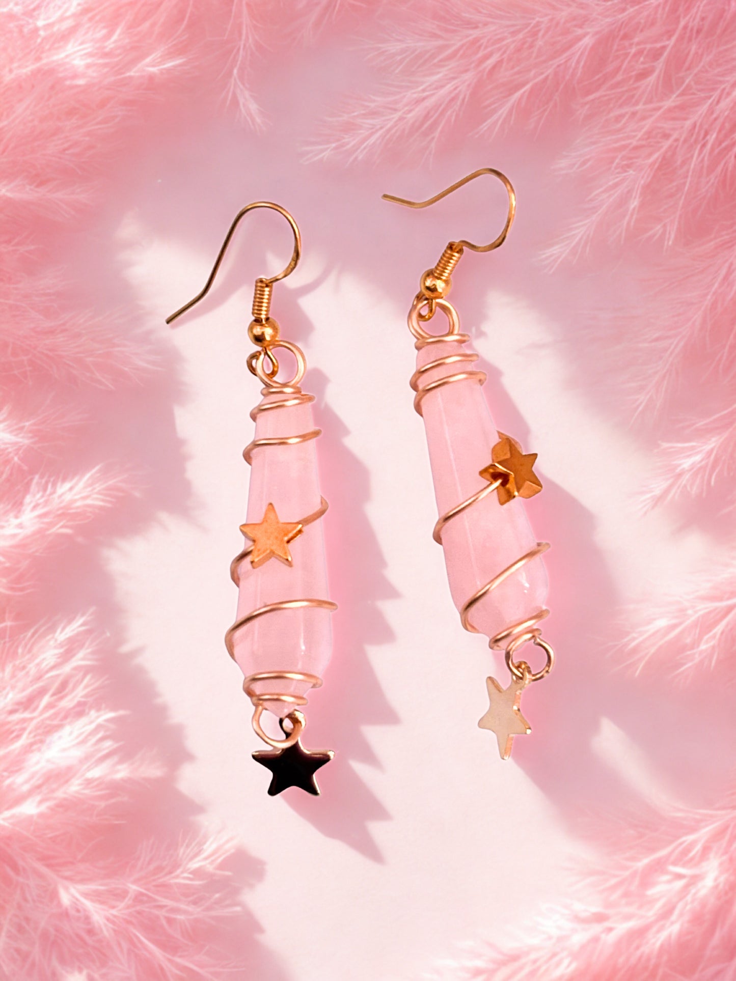 Pink rose quartz earrings with star charms on a pink fluffy background