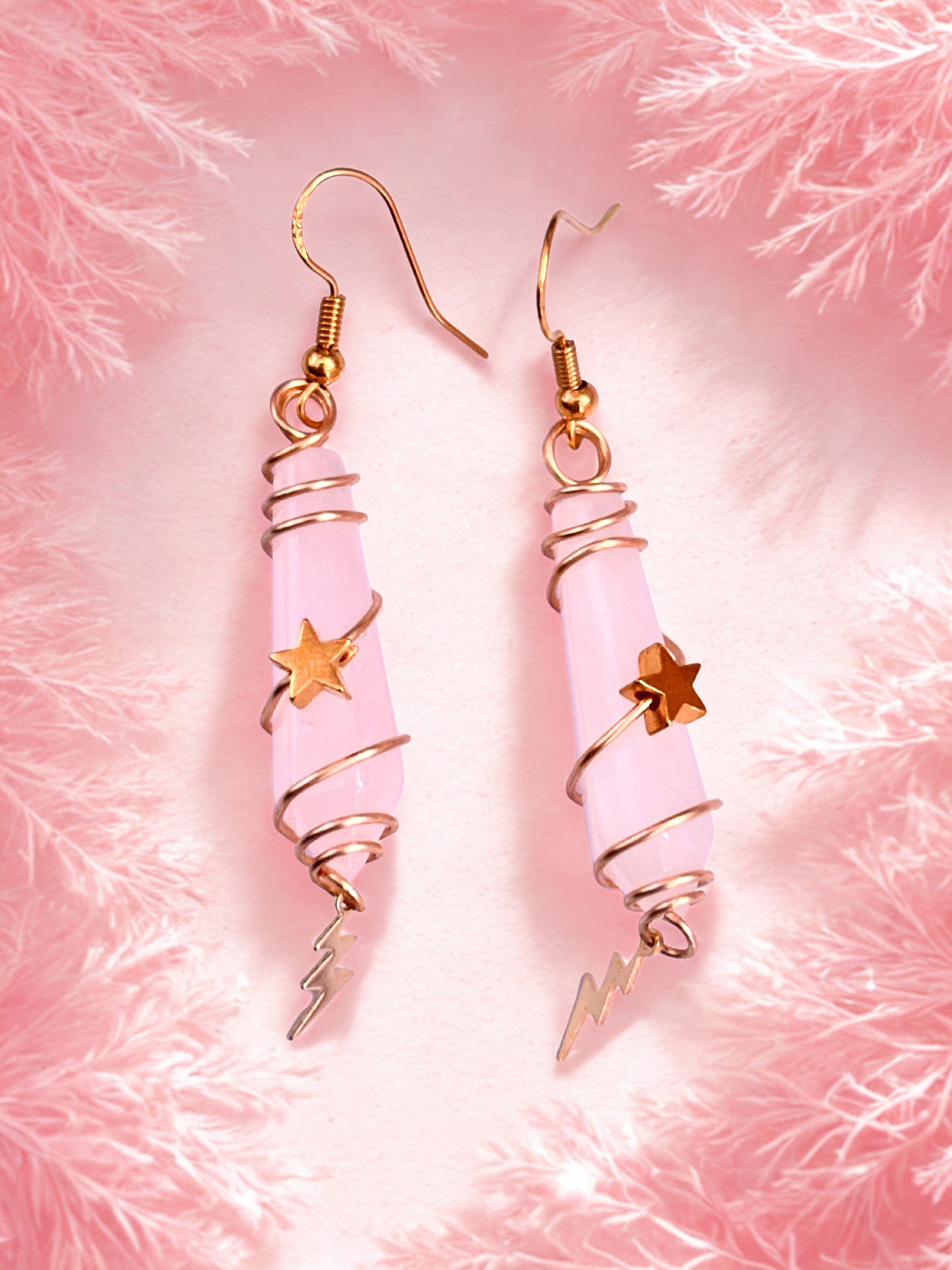 Pair of rose quartz earrings with pink and gold design on a pink fluffy background