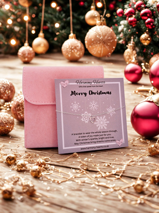 Pink jewelry box with a card on a wooden surface surrounded by Christmas decorations.