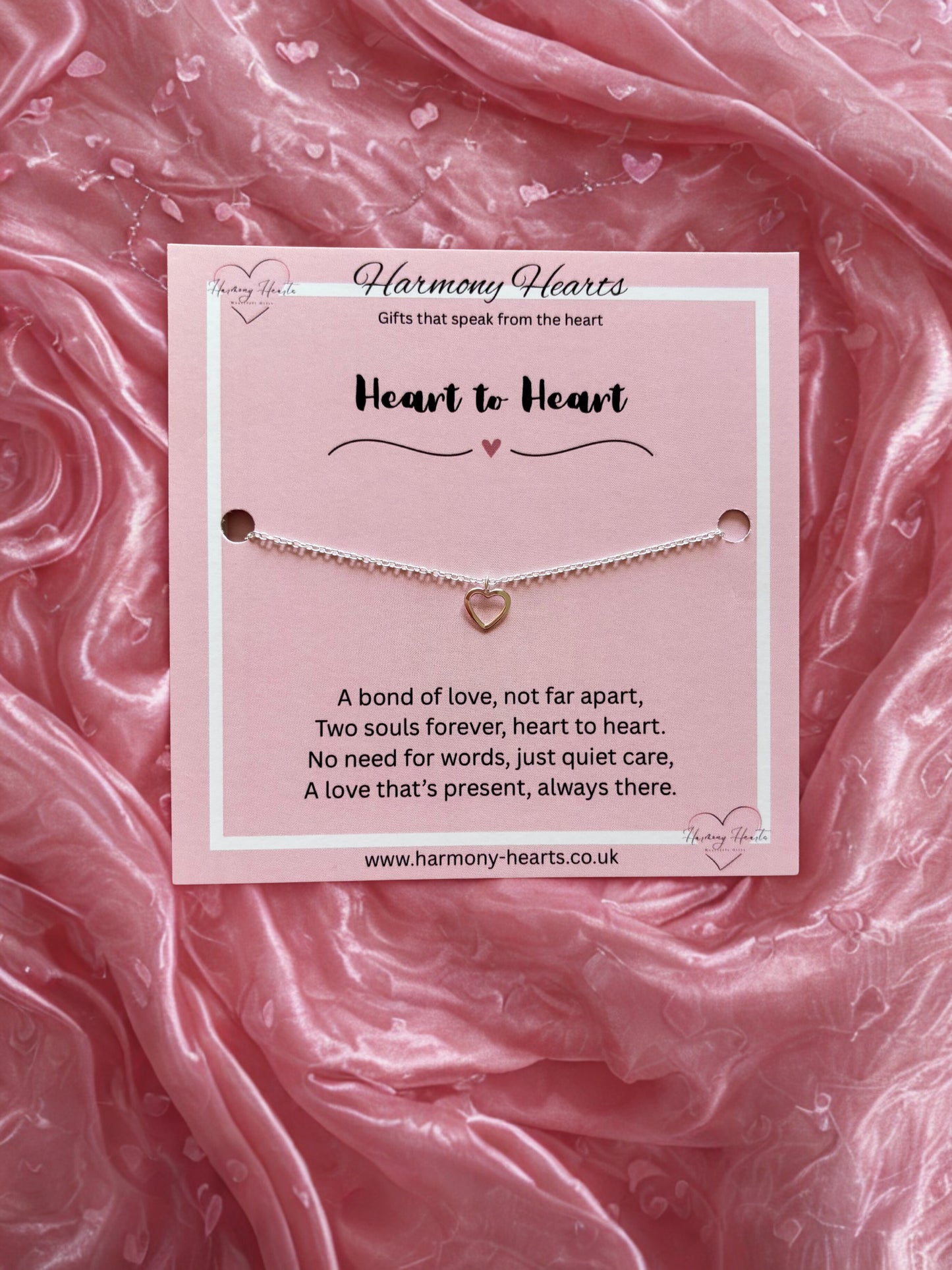 Bracelet with heart charm on a pink card against a pink fabric background