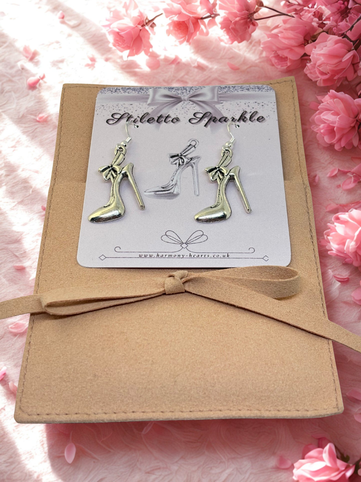 High-heeled shoe earrings on a card with a bow, surrounded by pink flowers.
