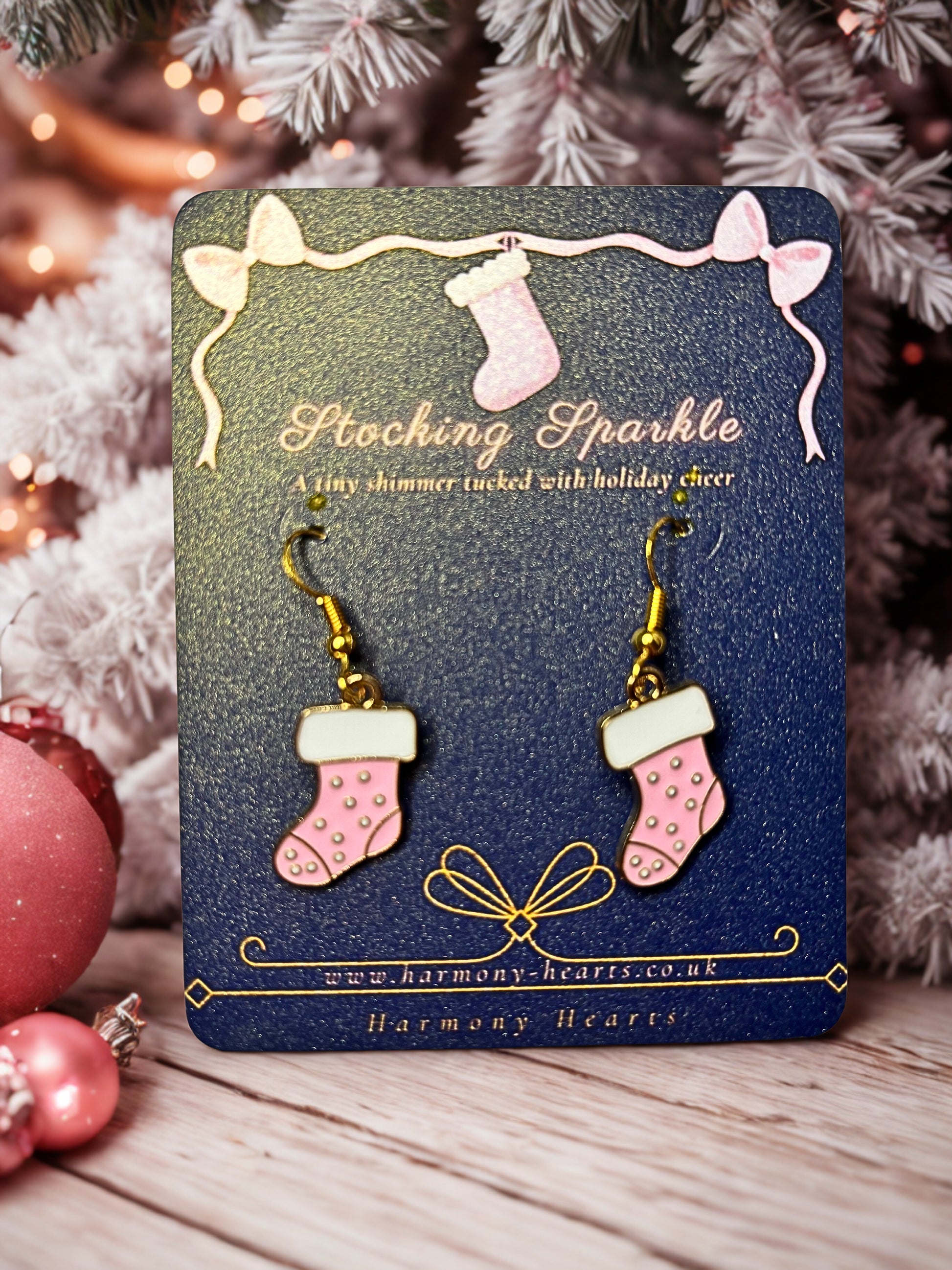 Pink stocking-shaped earrings on a blue card with Christmas tree and decorations in the background