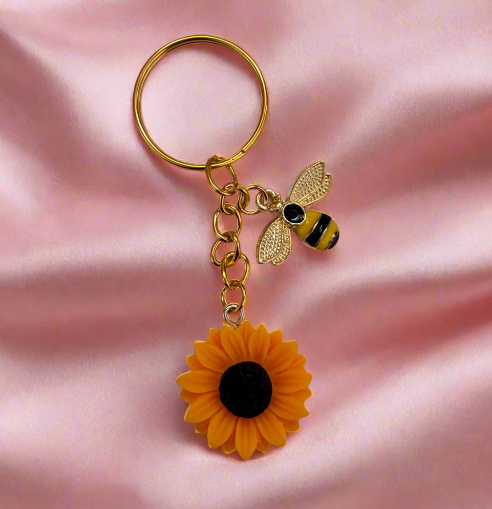 Keychain with bee and sunflower charm on a pink fabric background