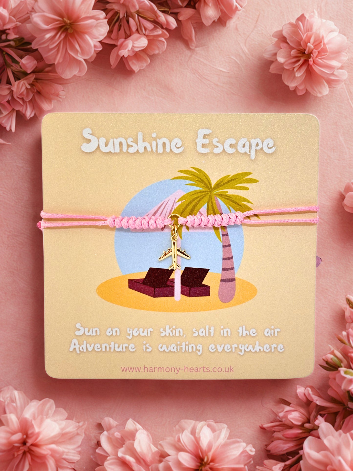 Pink cord bracelet with a gold plane charm presented on a Harmony Hearts branded card with  'Sunshine Escape' design on a pink floral background