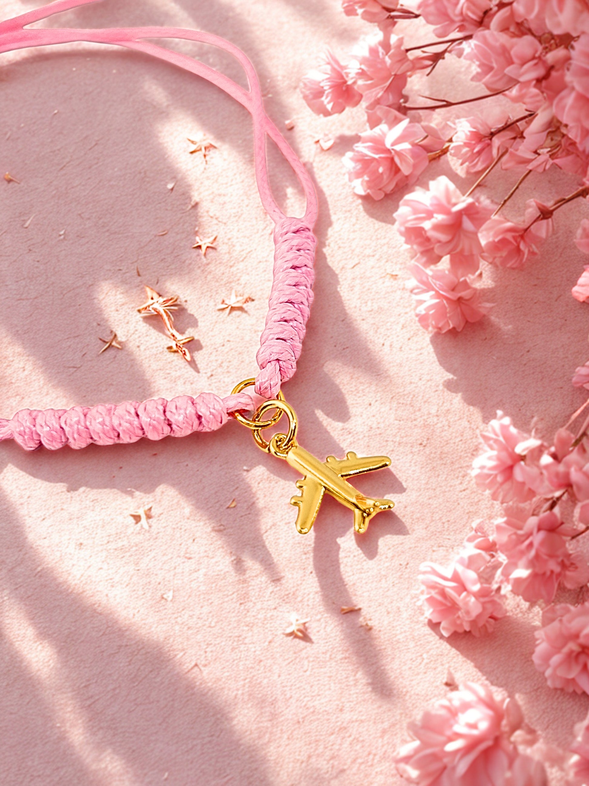 Pink braided bracelet with a gold airplane charm on a pink floral background