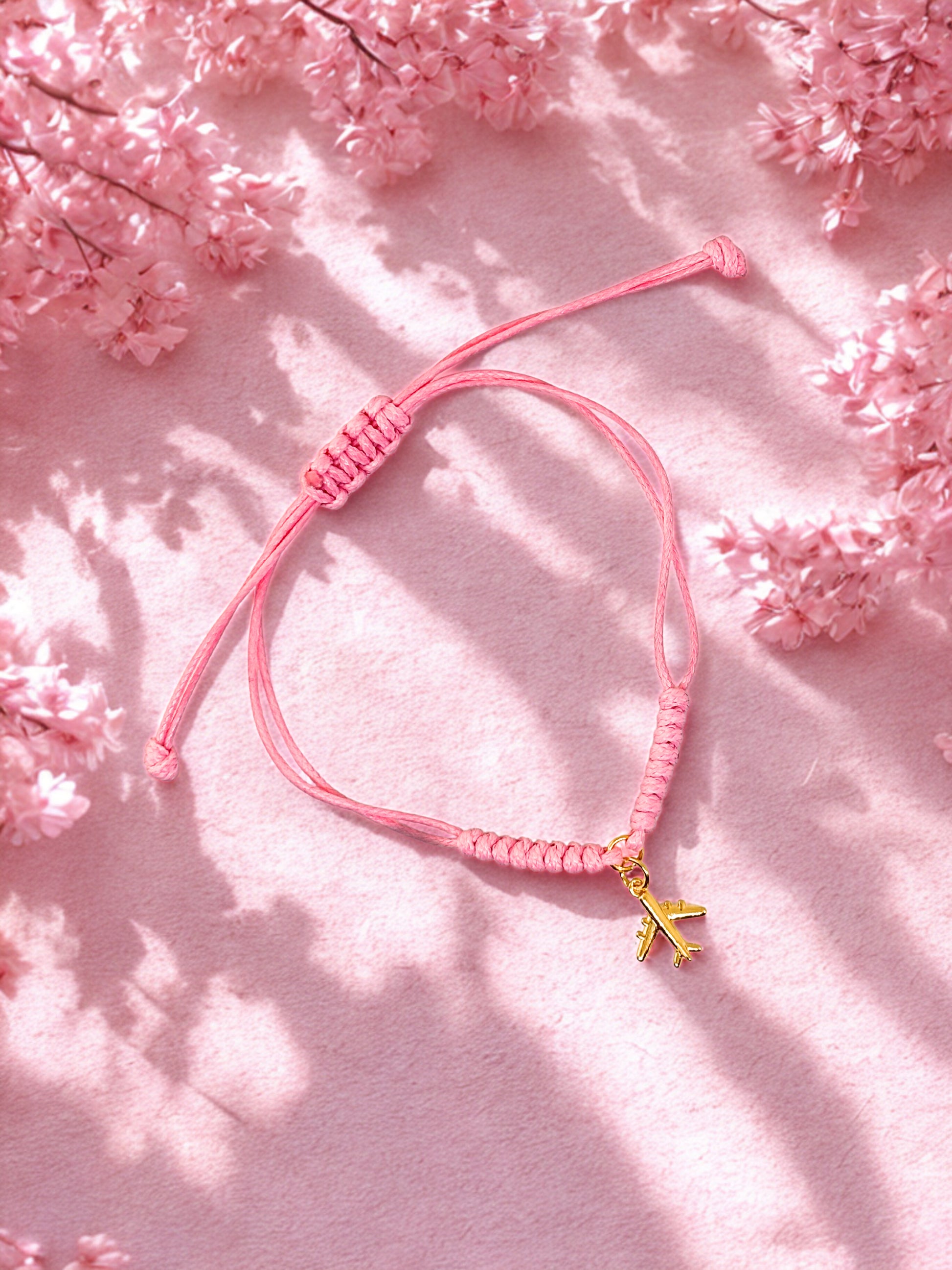 Pink bracelet with a gold airplane charm on a pink floral background