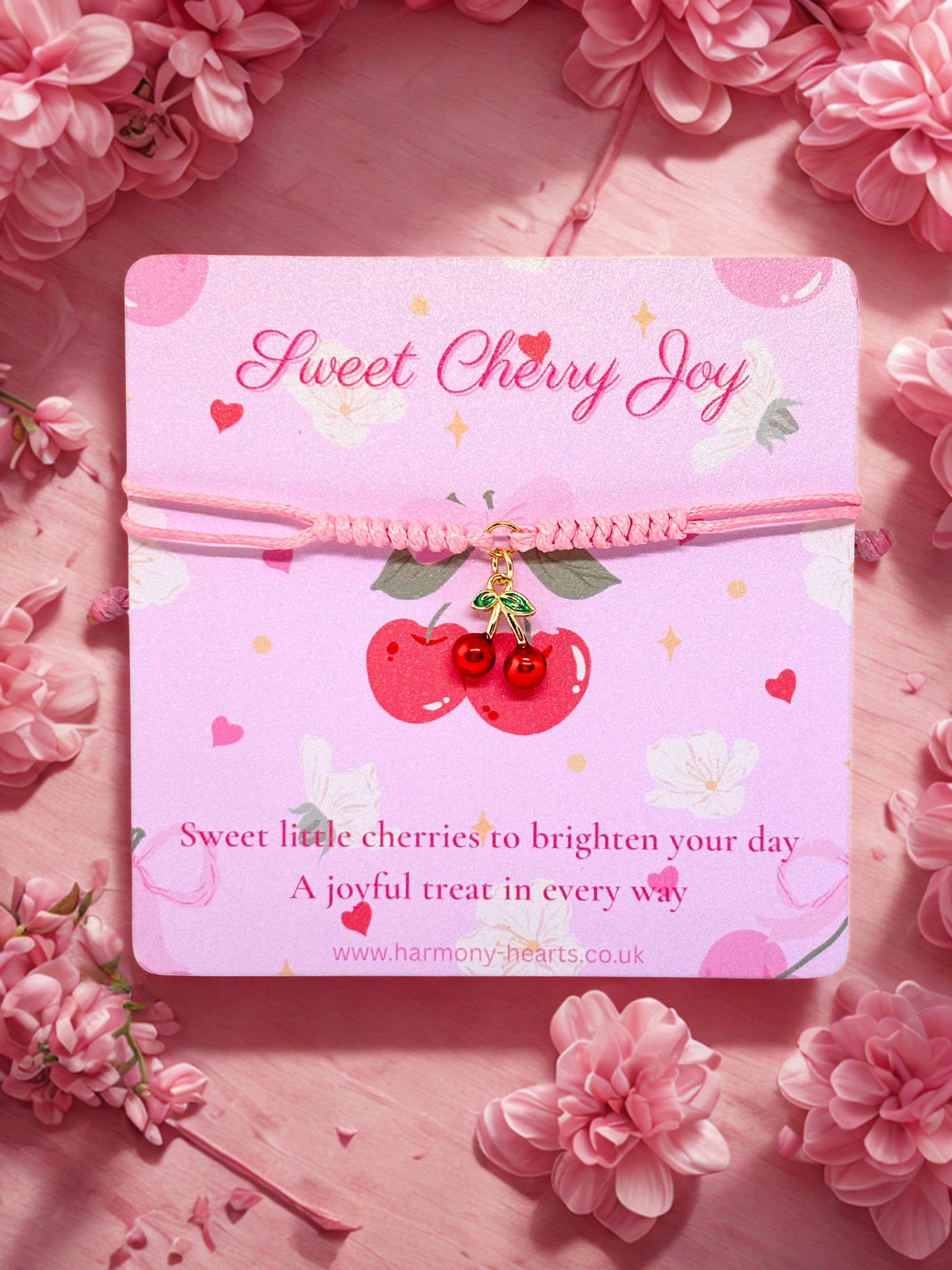 Pink cord bracelet with cherry charm on a cherry themed card on a pink floral background