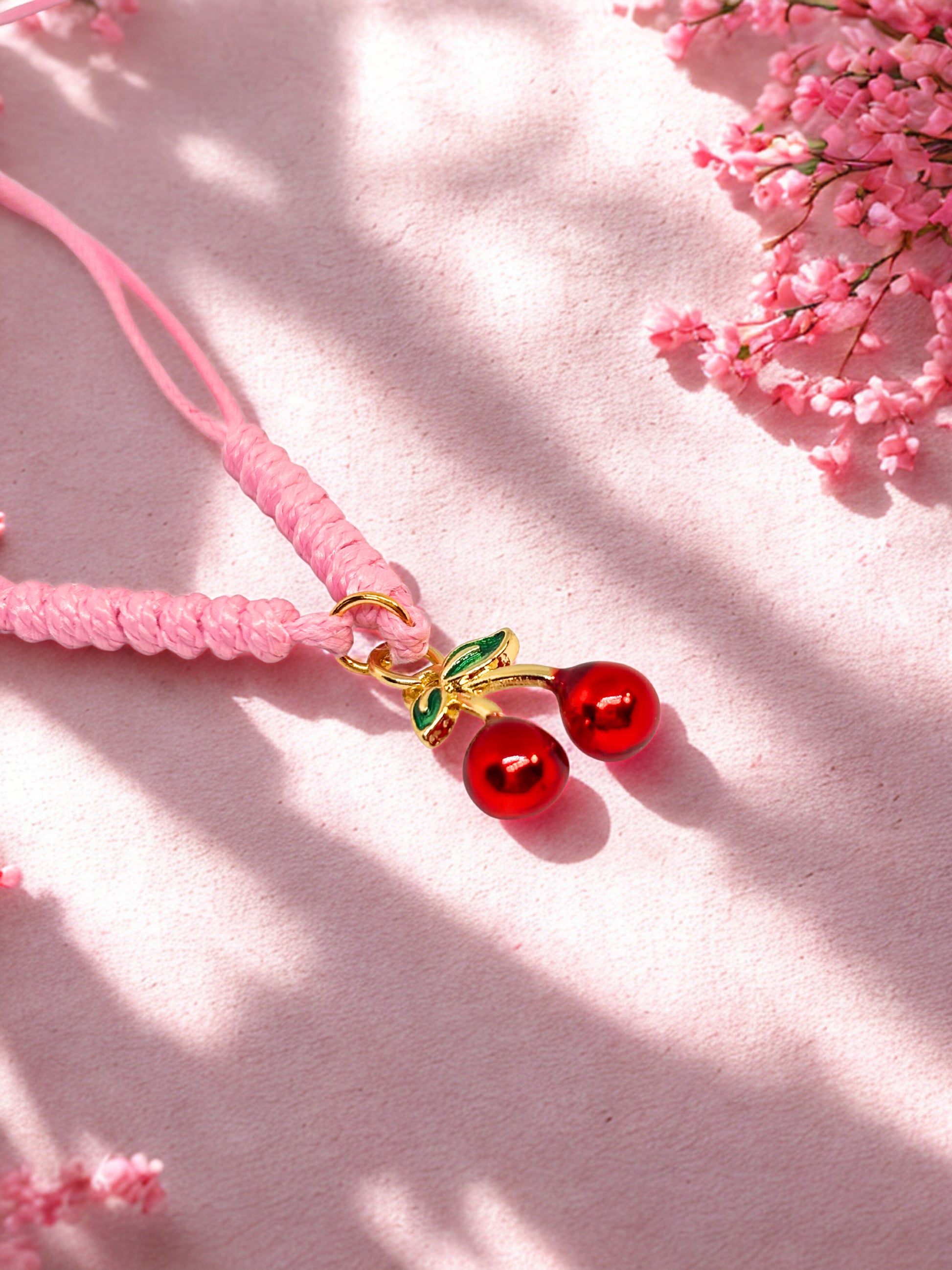 Pink cord bracelet with cherry charm on a pink background