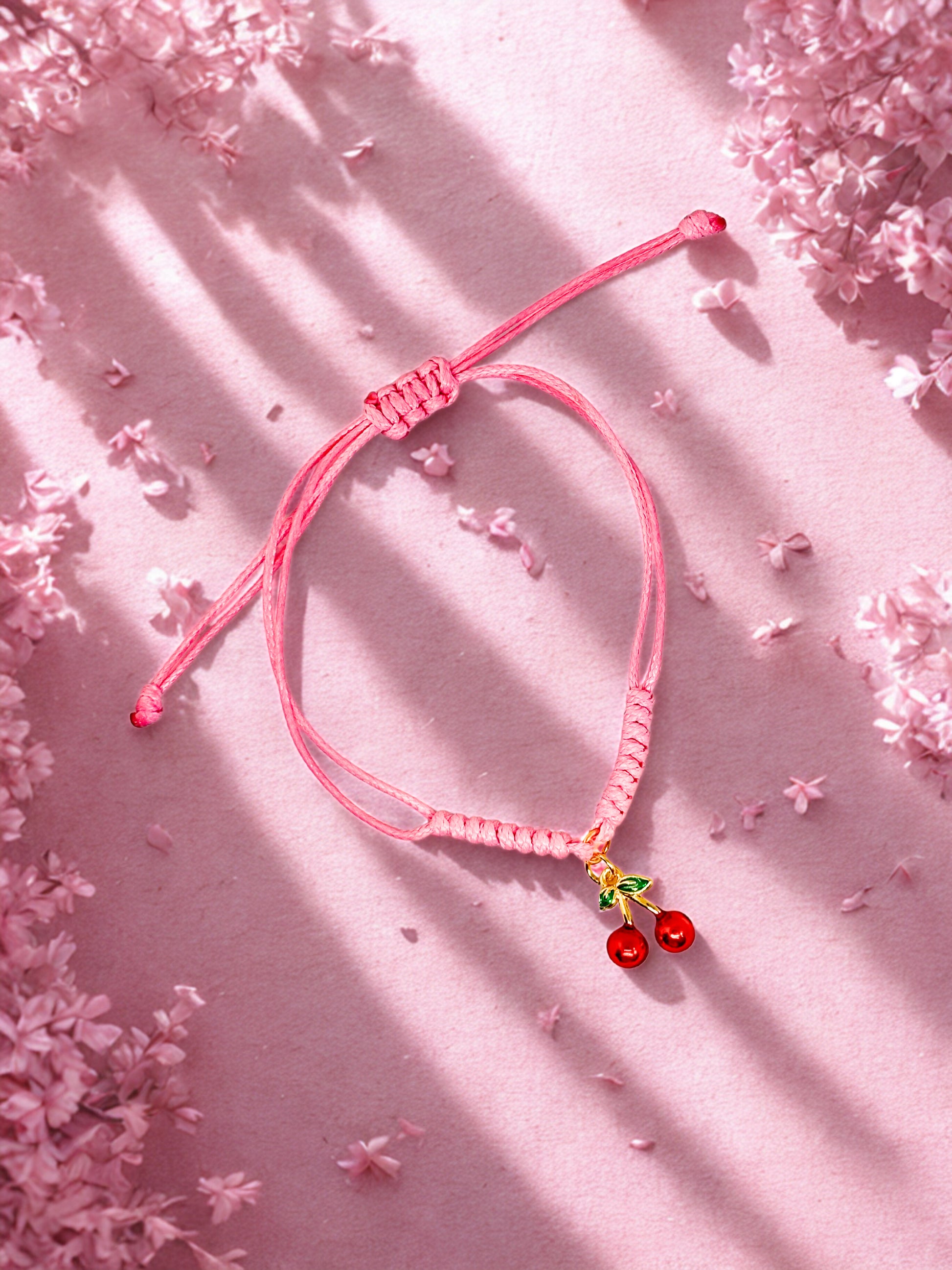 Pink bracelet with cherry charm on a pink background with cherry blossoms.