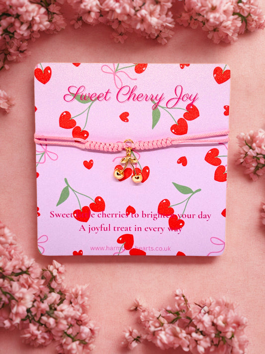 Pink cord bracelet with a gold cherry charm presented on a Harmony Hearts branded poem card