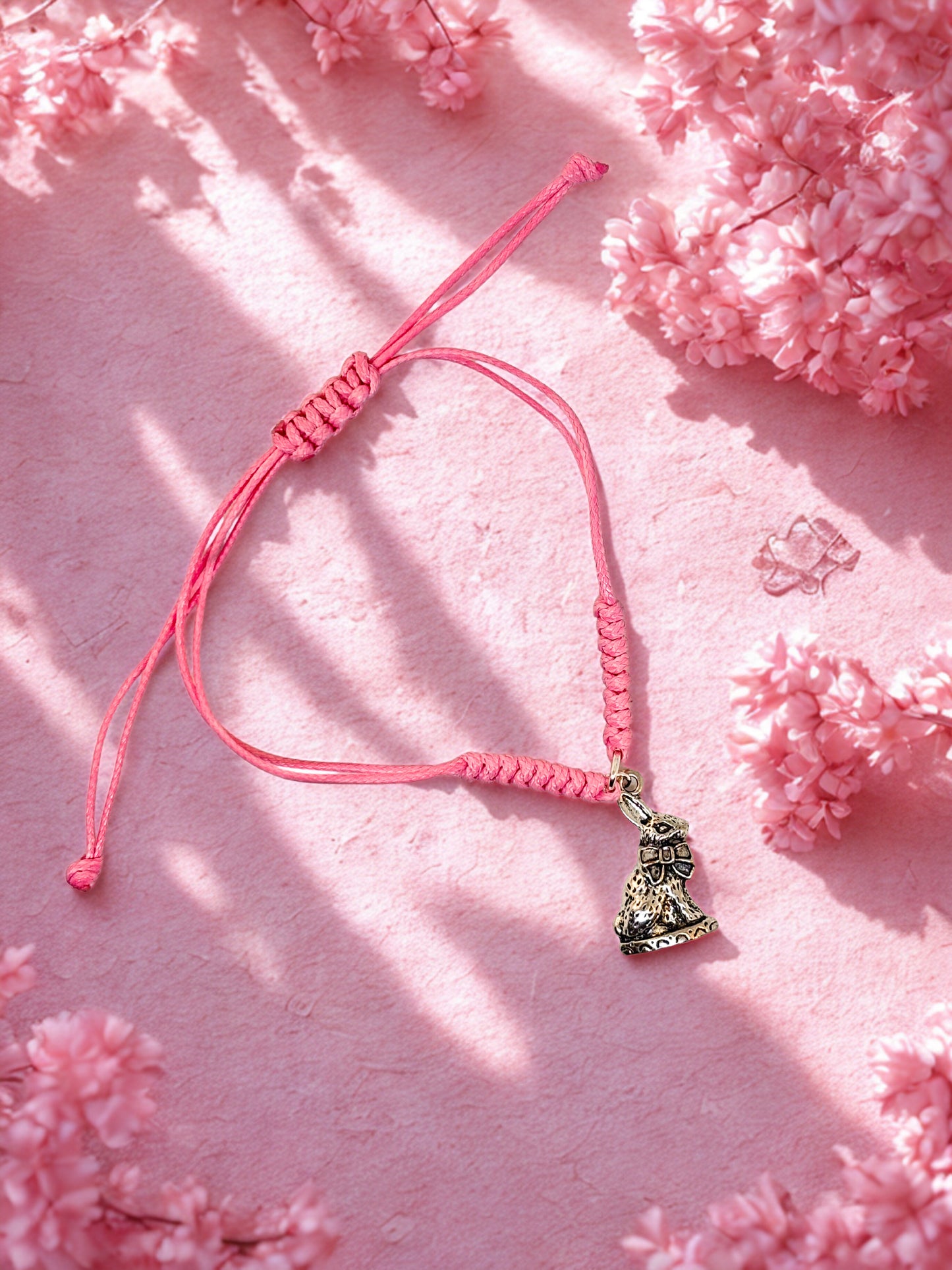 Pink cord bracelet with a bunny charm on a pink floral background
