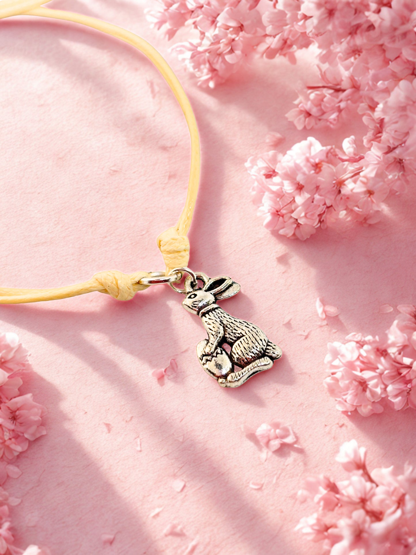 beige cord bracelet with a bunny charm on a pink floral background