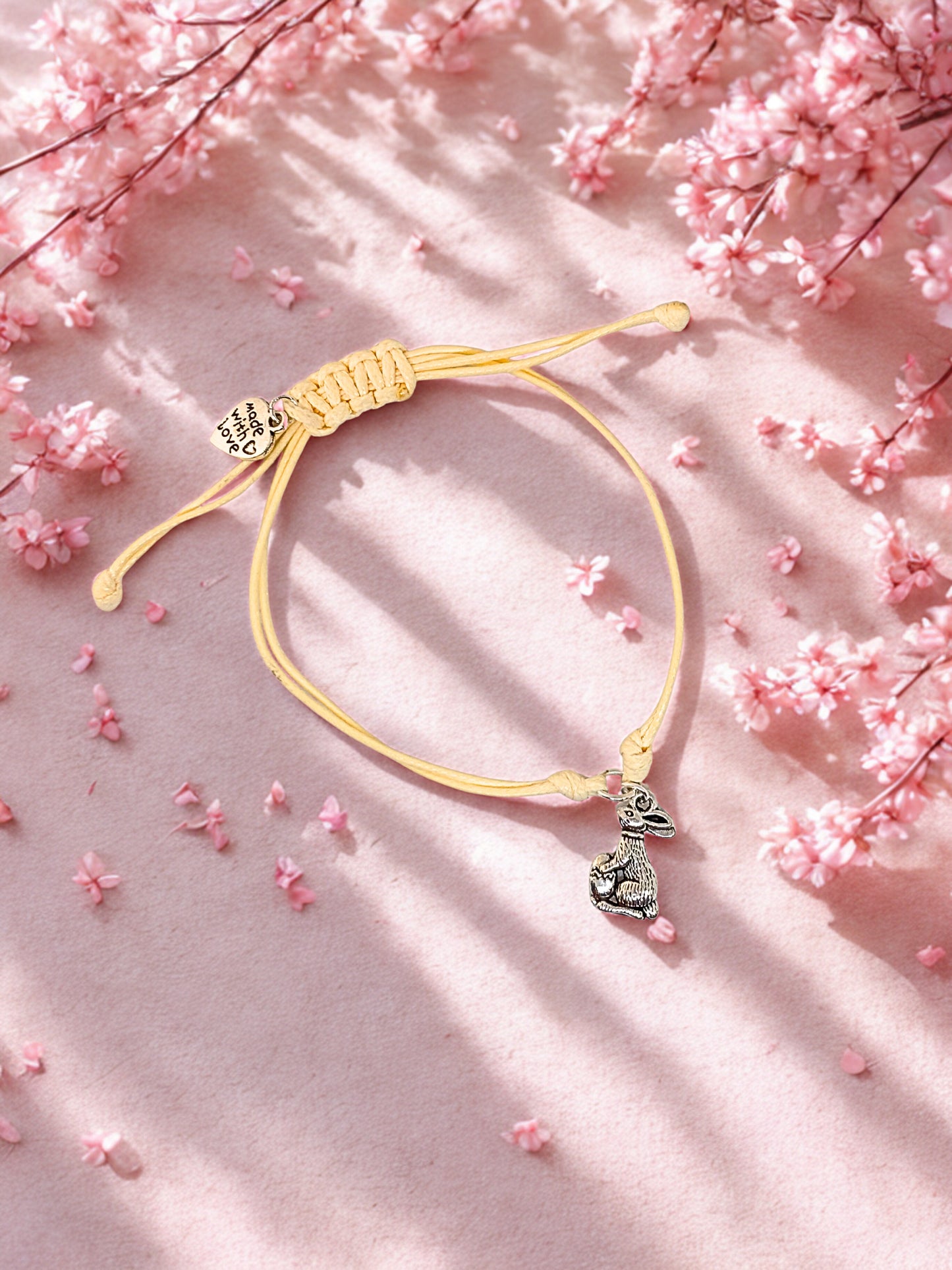 Beige bracelet with a silver bunny charm on a pink floral background