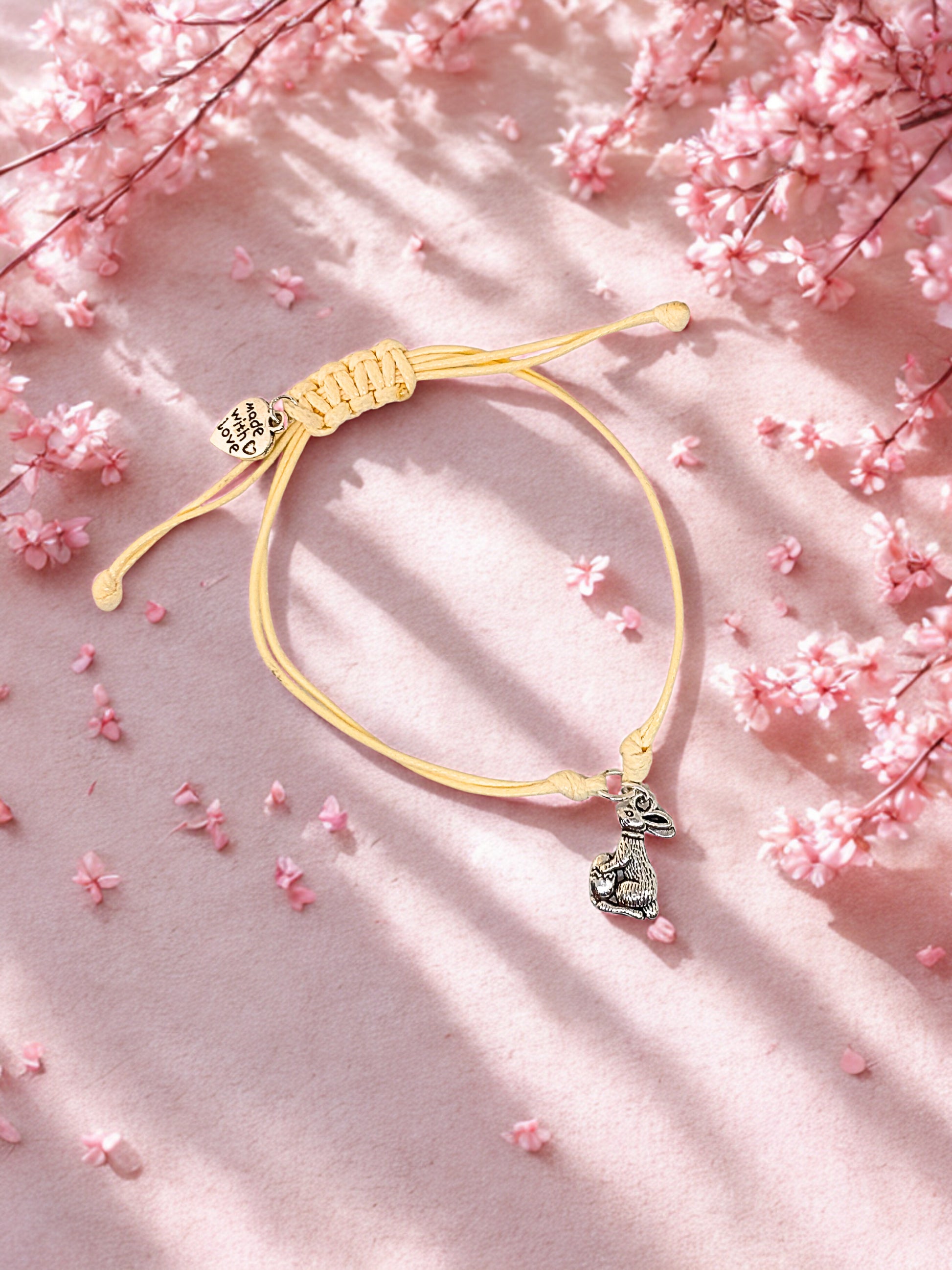 Beige bracelet with a silver bunny charm on a pink floral background