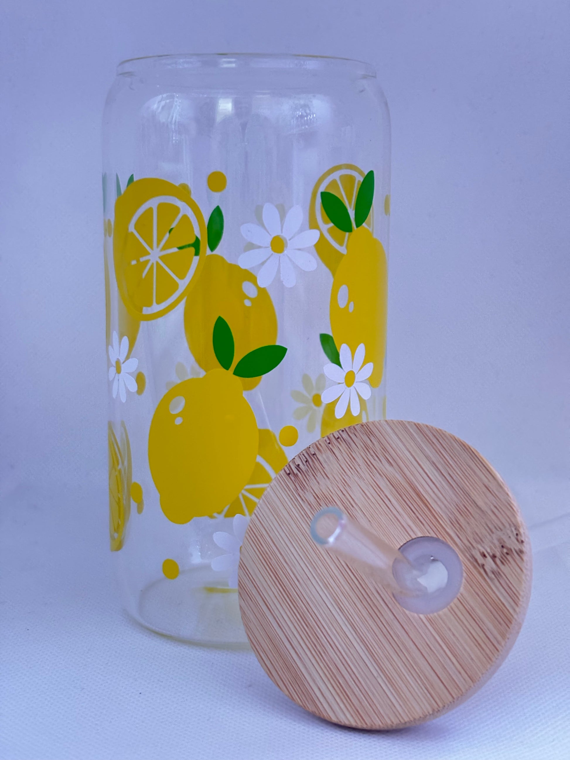 Clear glass tumbler with lemon design and wooden lid on a light purple background