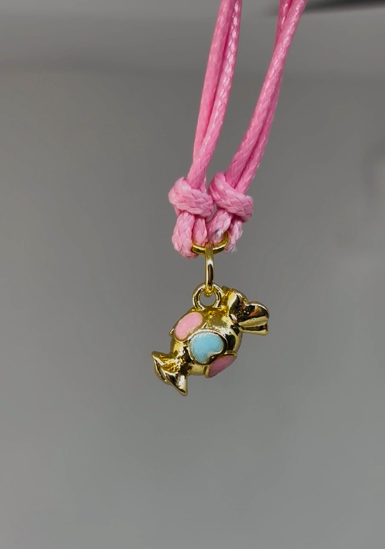 Gold sweet charm with enamel hearts on a pink cord