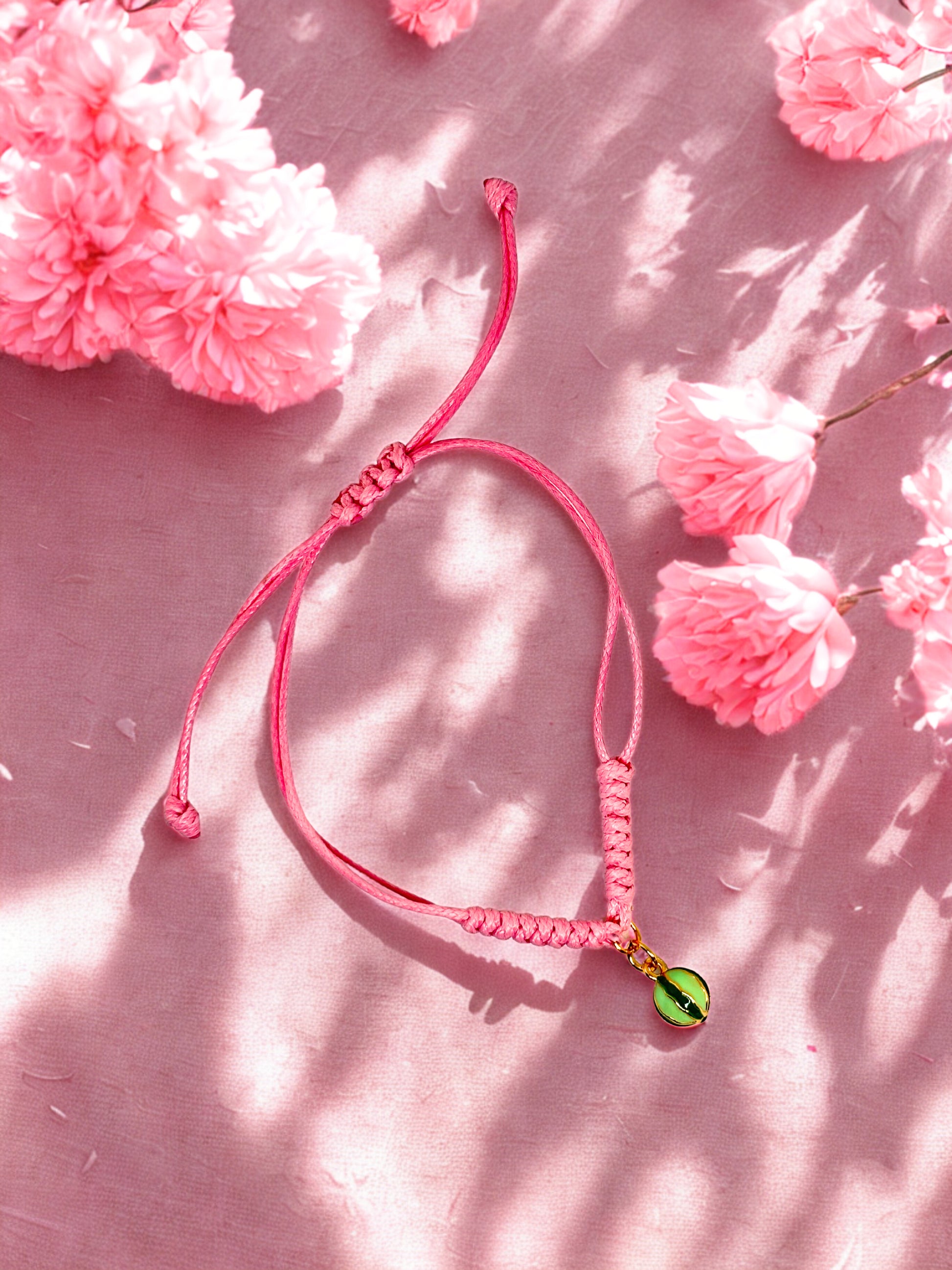 Pink braided bracelet with a green and gold watermelon charm on a pink floral background