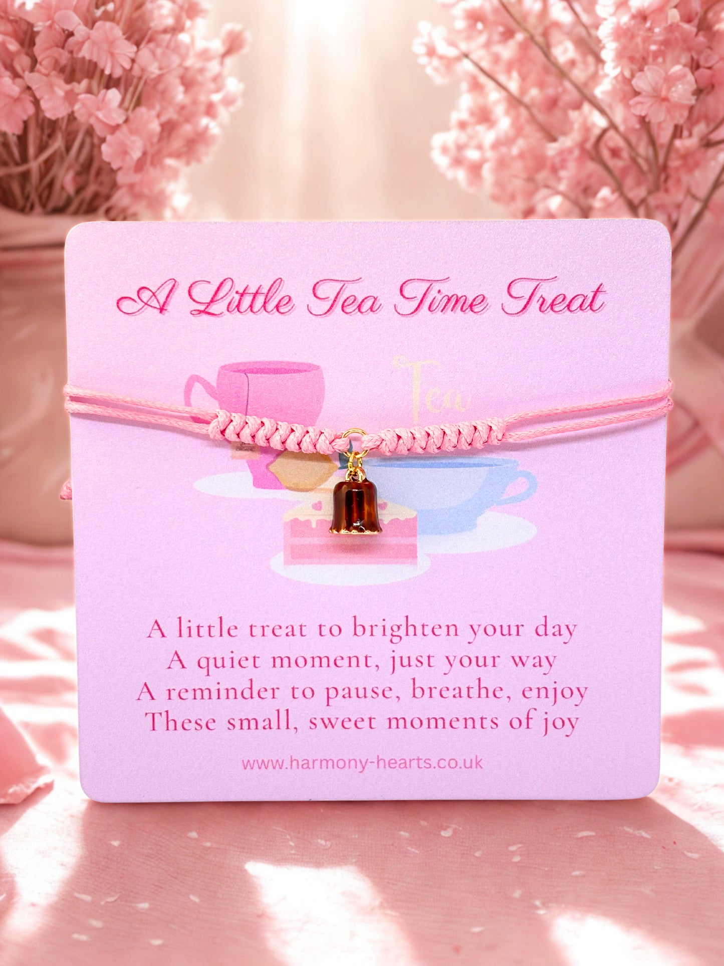 Pink cord bracelet with a dessert charm presented on a Harmony Hearts branded card with tea-themed charm and text on a soft pink background