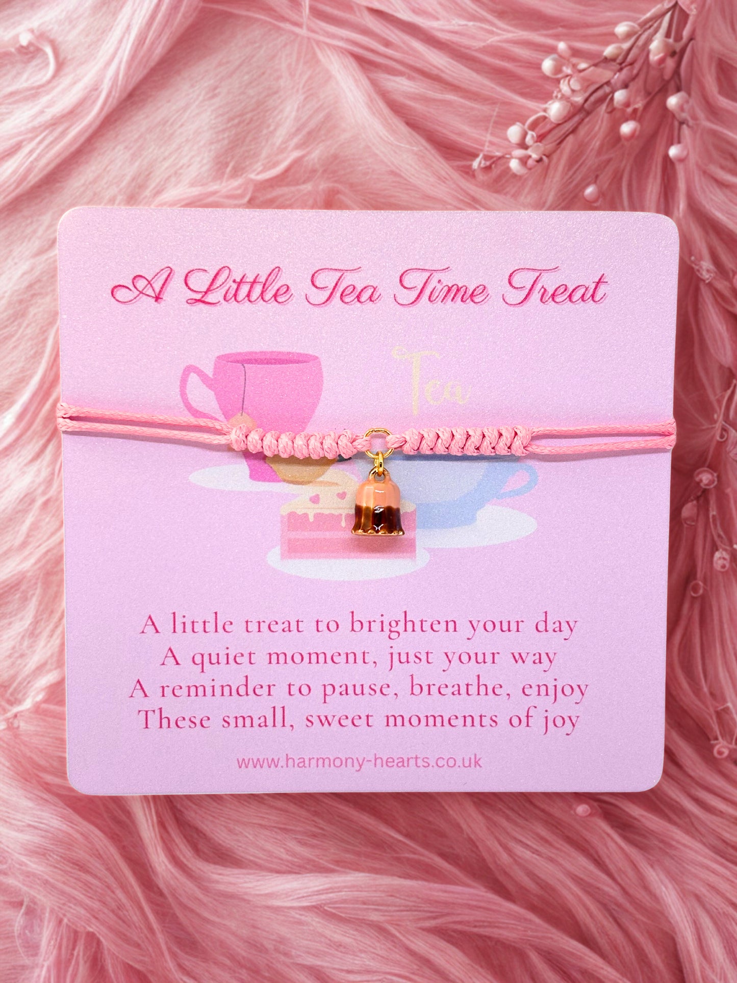 Pink cord bracelet with a dessert charm presented on a branded Harmony Hearts card with tea cup design and text on a pink textured background