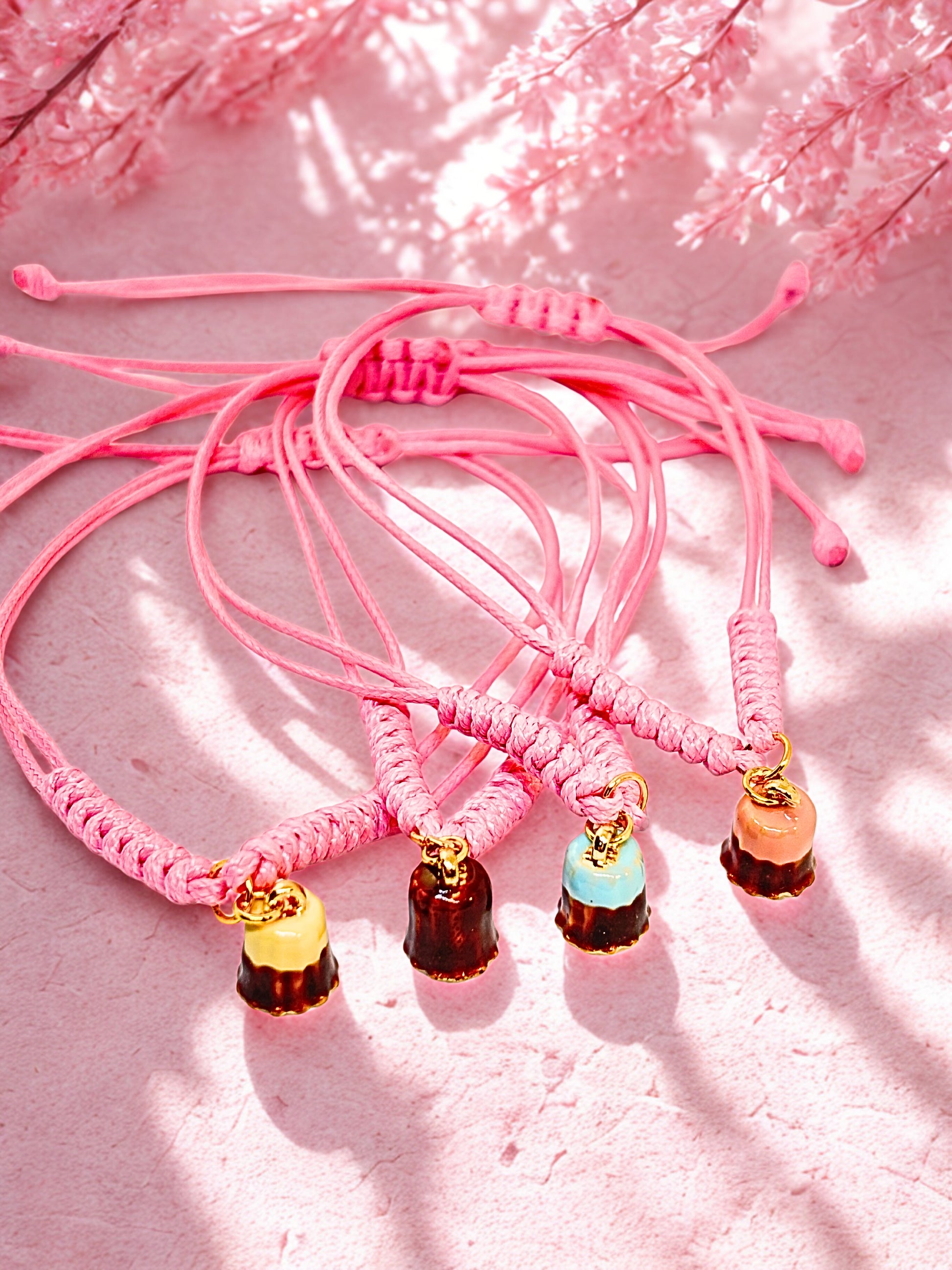 Pink corded bracelets with pudding dessert inspired charms on a pink floral background