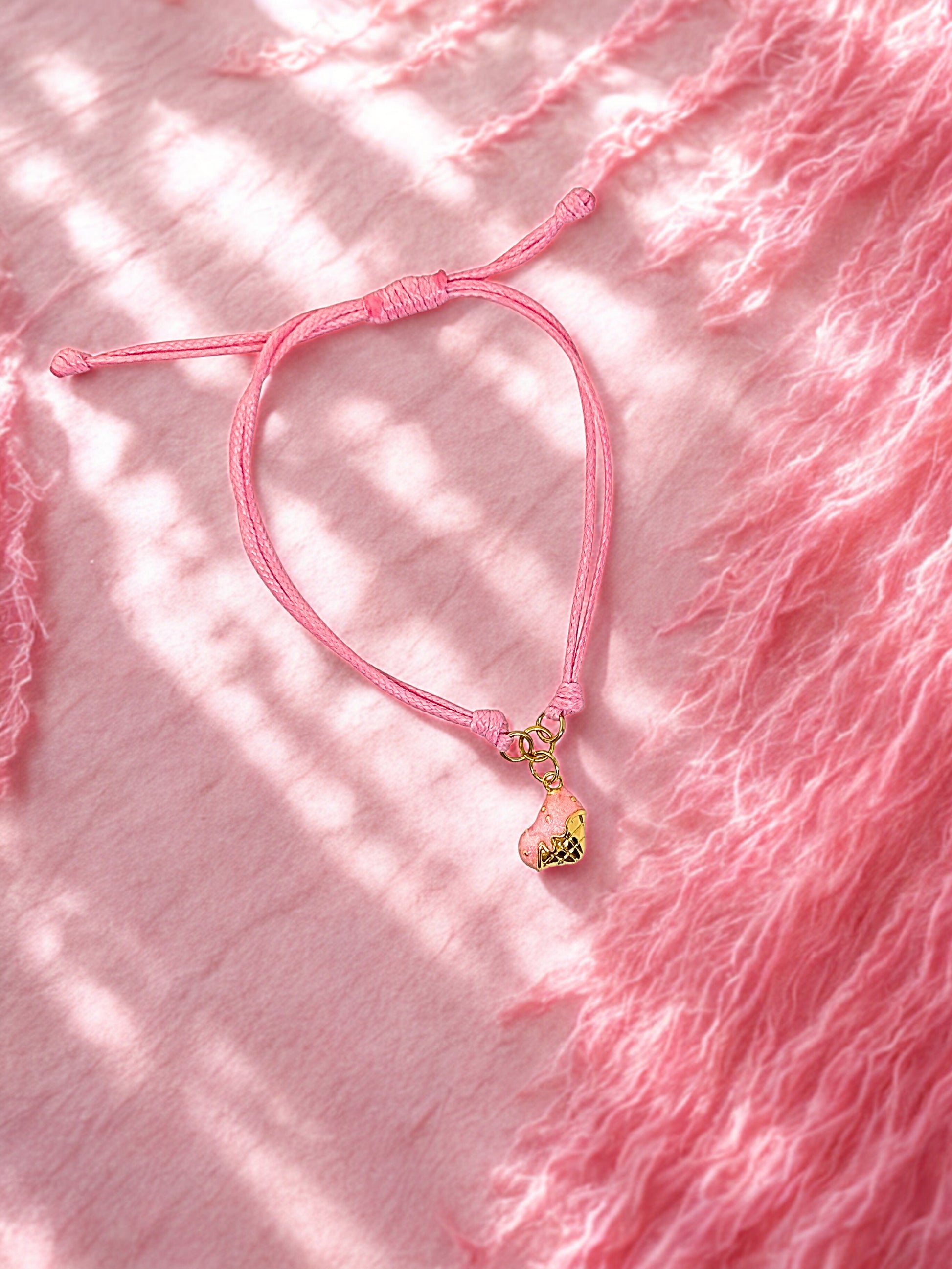 Pink bracelet with a gold heart charm on a pink textured fabric background