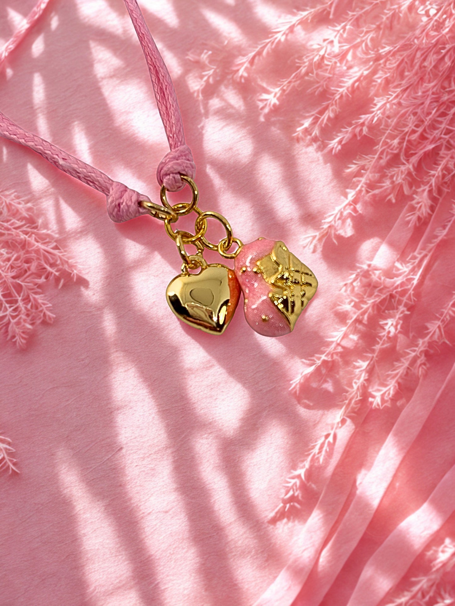 Pink cord with gold heart-shaped charms on a pink textured background