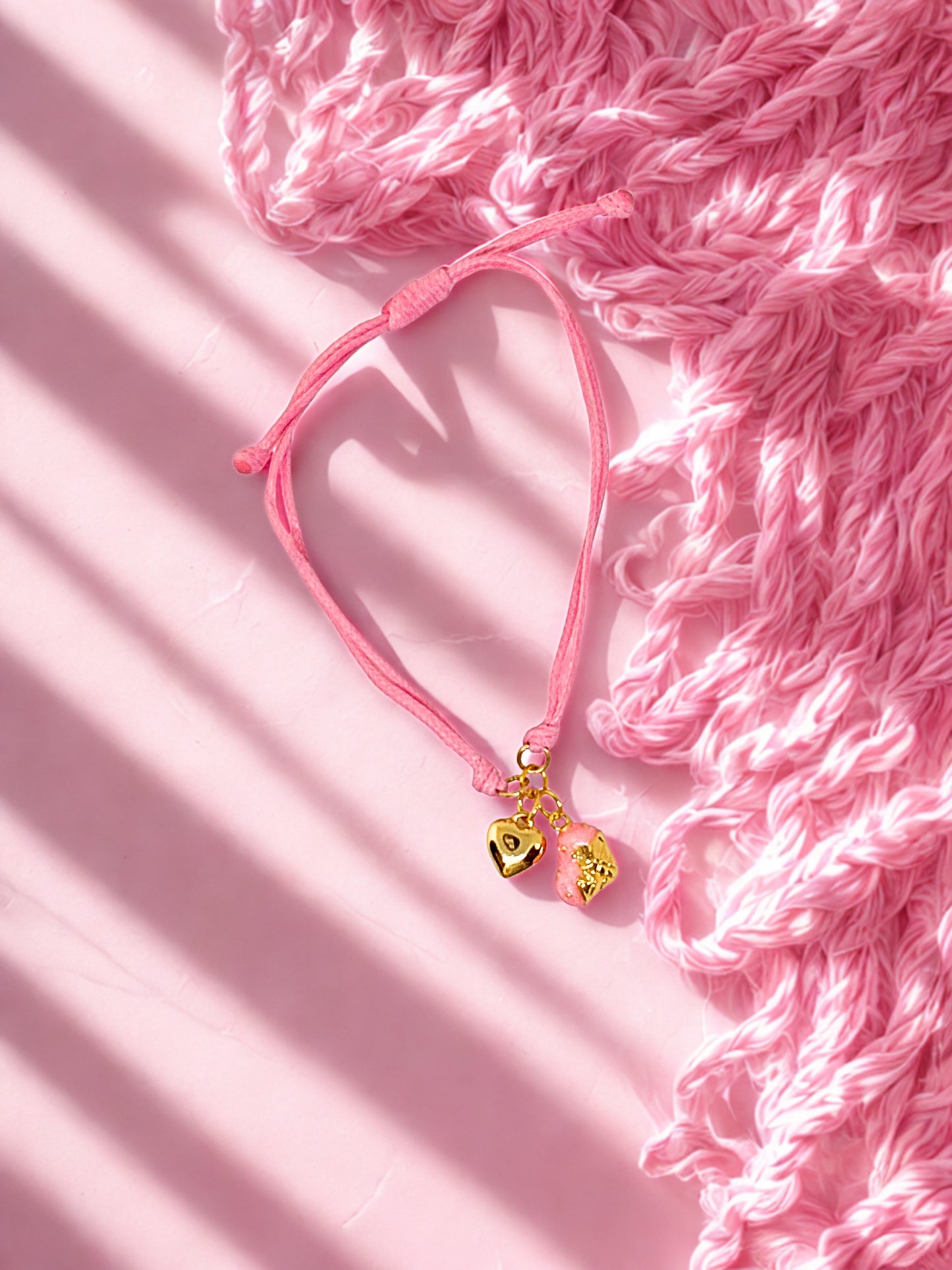 Pink bracelet with a gold charm on a pink textured background