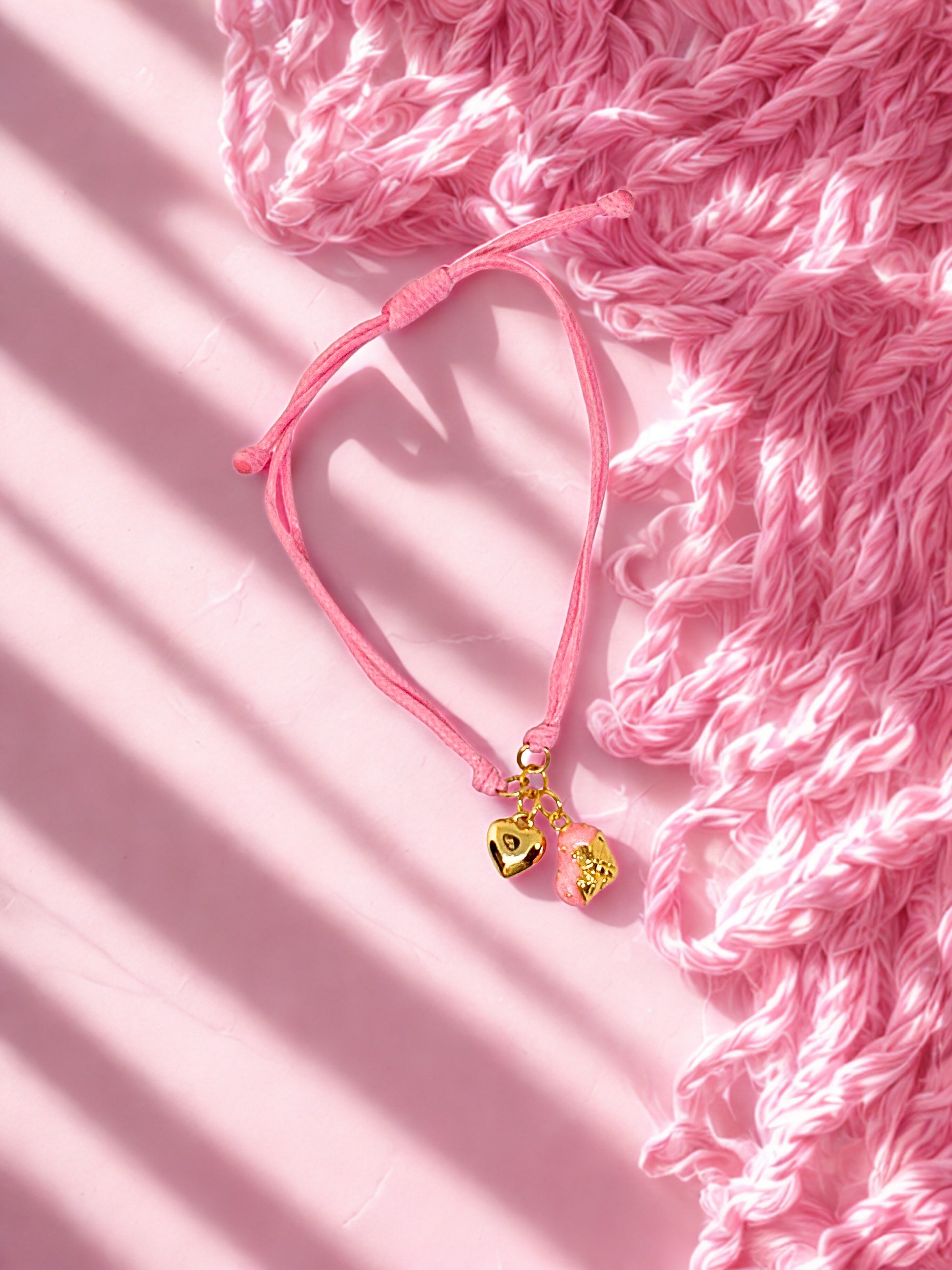 Pink bracelet with a gold charm on a pink textured background