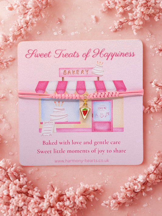 Slice of cake charm bracelet preseneted on a pink bakery-themed card with cherry blossoms on a pink background