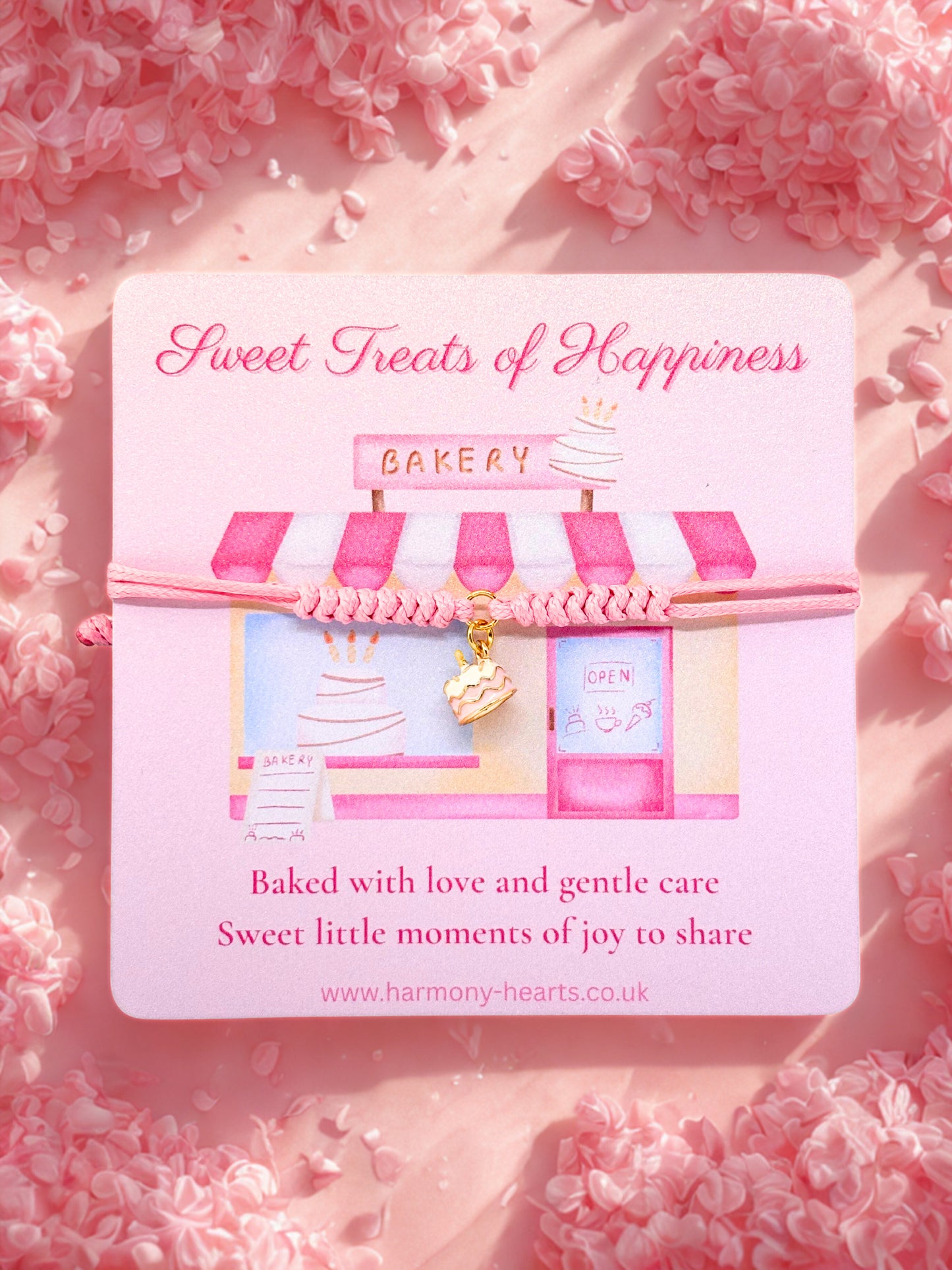 Cake charm bracelet present on a card with bakery design and 'Sweet Treats of Happiness' text on a pink floral background