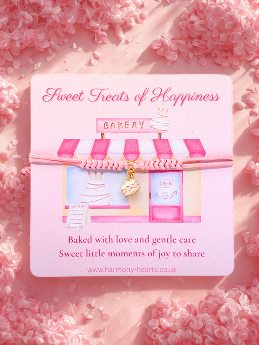 Cake charm bracelet present on a card with bakery design and 'Sweet Treats of Happiness' text on a pink floral background
