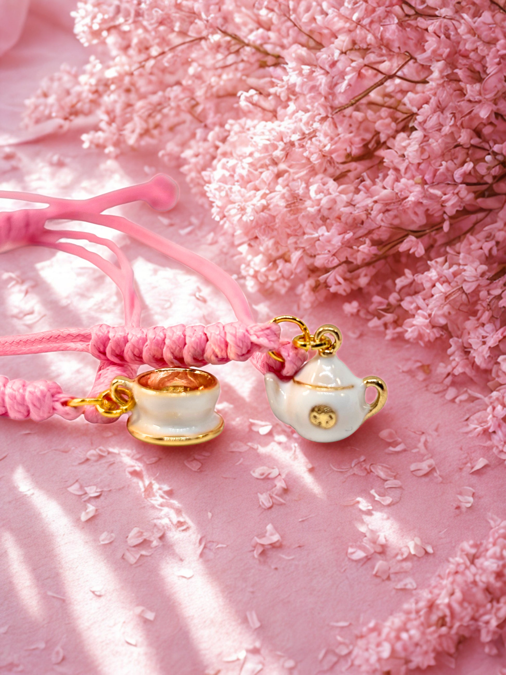 Pink braided cords with teapot and teacup shaped charms on a pink floral background