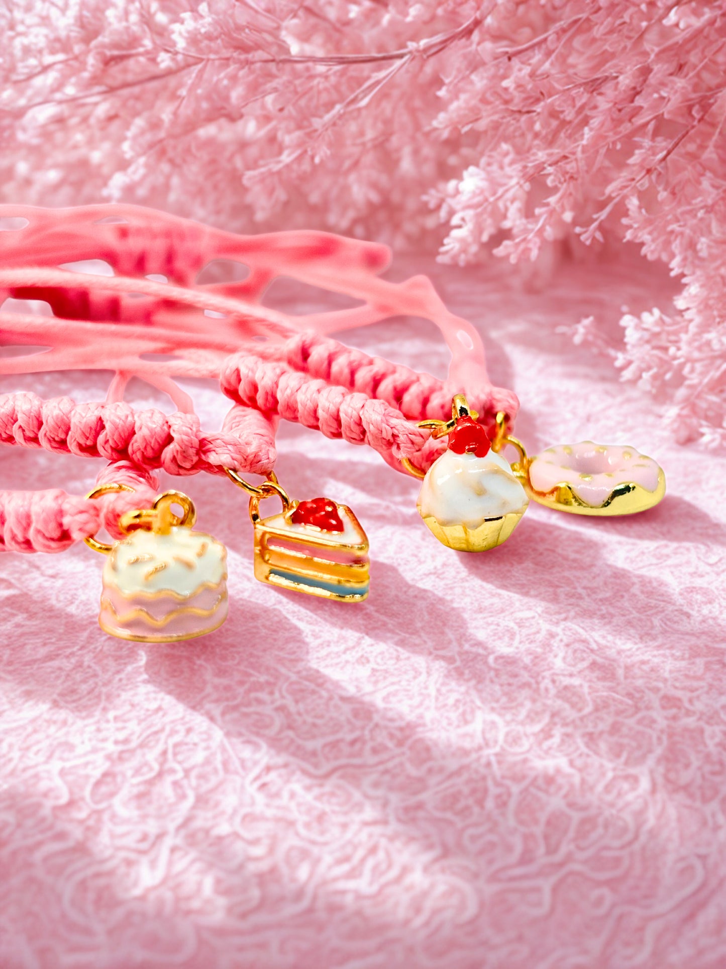 Pink braided bracelets with cake-shaped charms on a pink textured backgrounds 